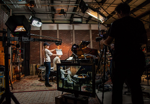 Behind the scenes of a video or film shoot with crew preparing scene, cameras, and lighting setup in a studio.