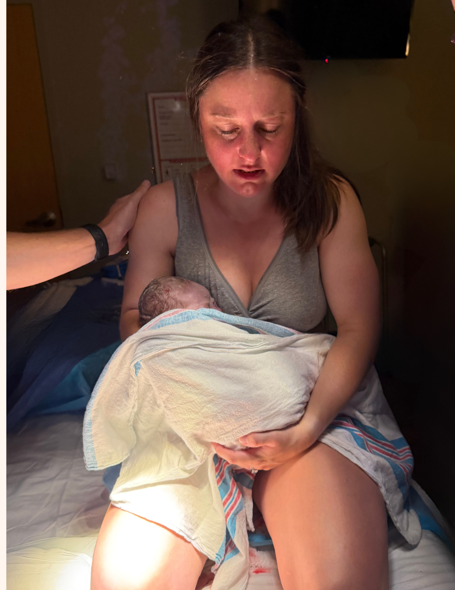 A woman holding a newborn baby after birth in a hospital room, with a man touching her shoulder in a supportive gesture.