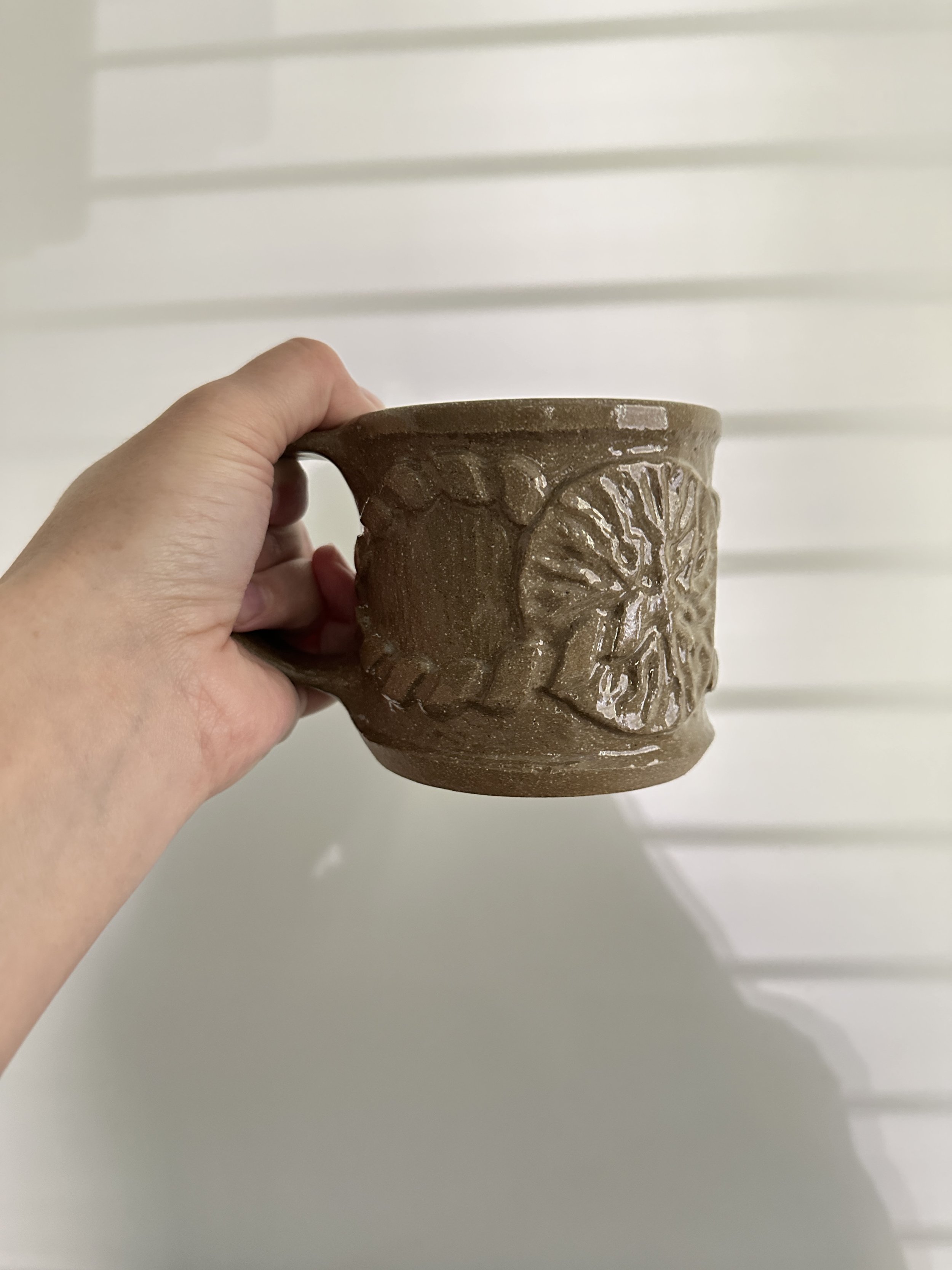 A person's hand holding a brown ceramic mug with a placenta design.