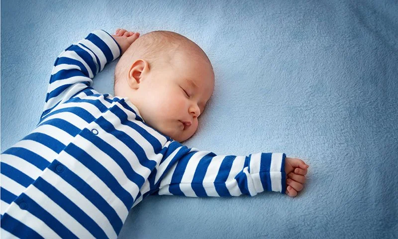 Baby sleeping in blue and white striped outfit on blue blanket