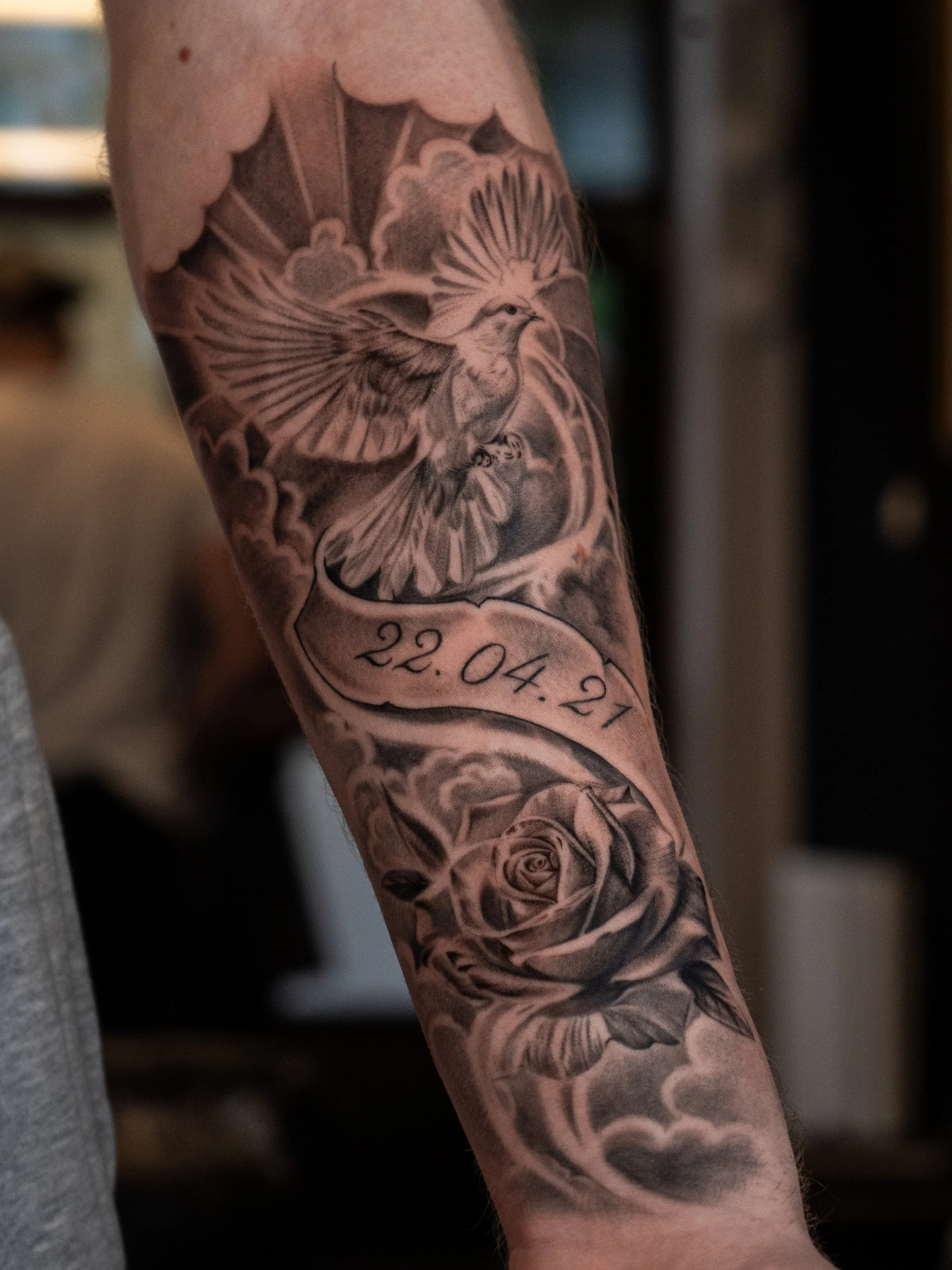 Tatuerad fågel och ros med datum 22.04.21 på armen.