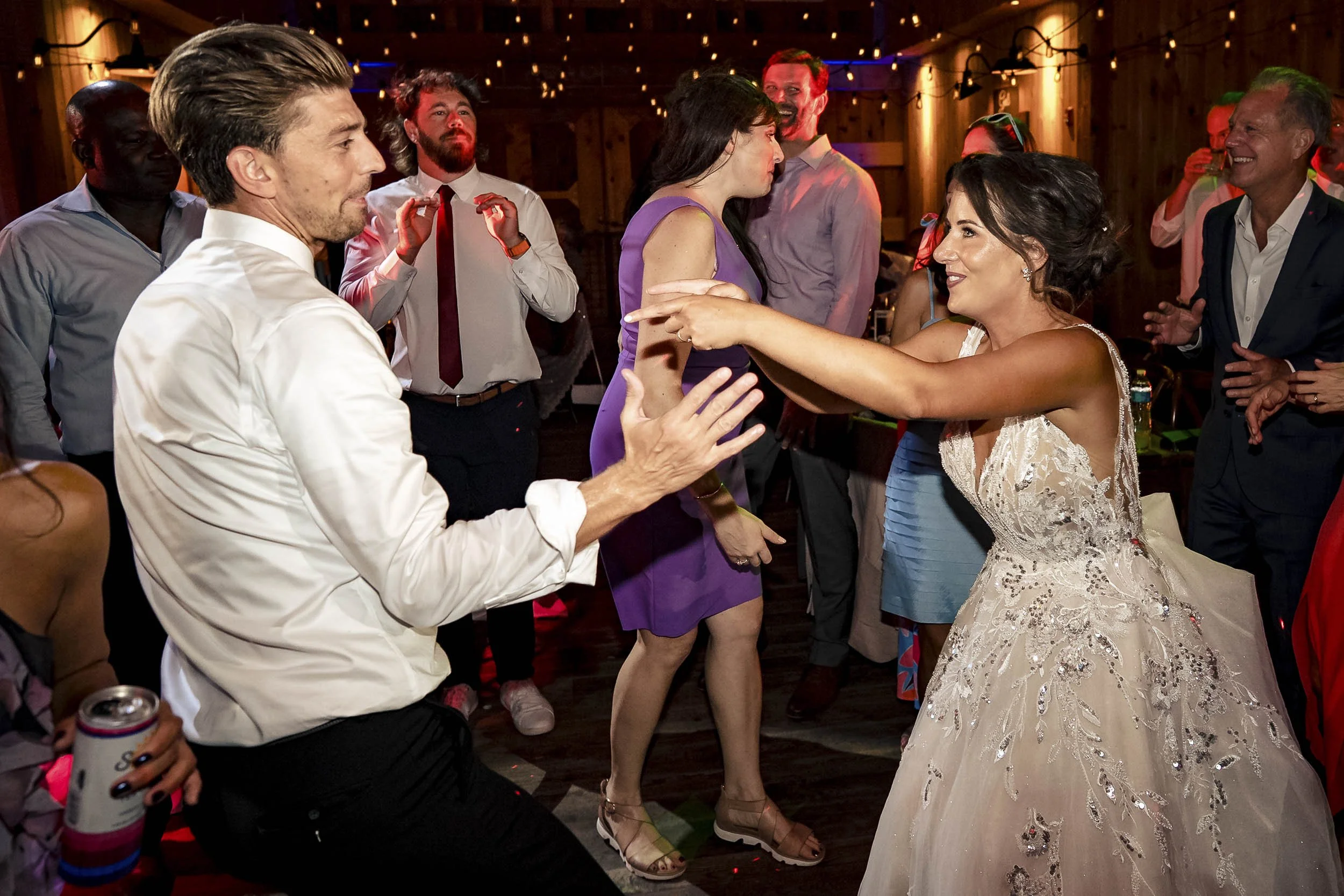 Sarah and Andrew smiling and dancing together among guests at their wedding reception.