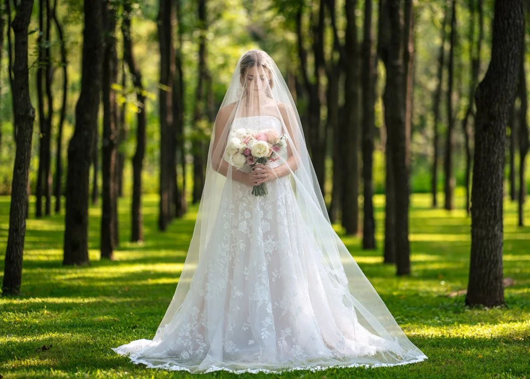 `Bride standing among sunlit trees during a summer wedding in Manassas, Virginia.`