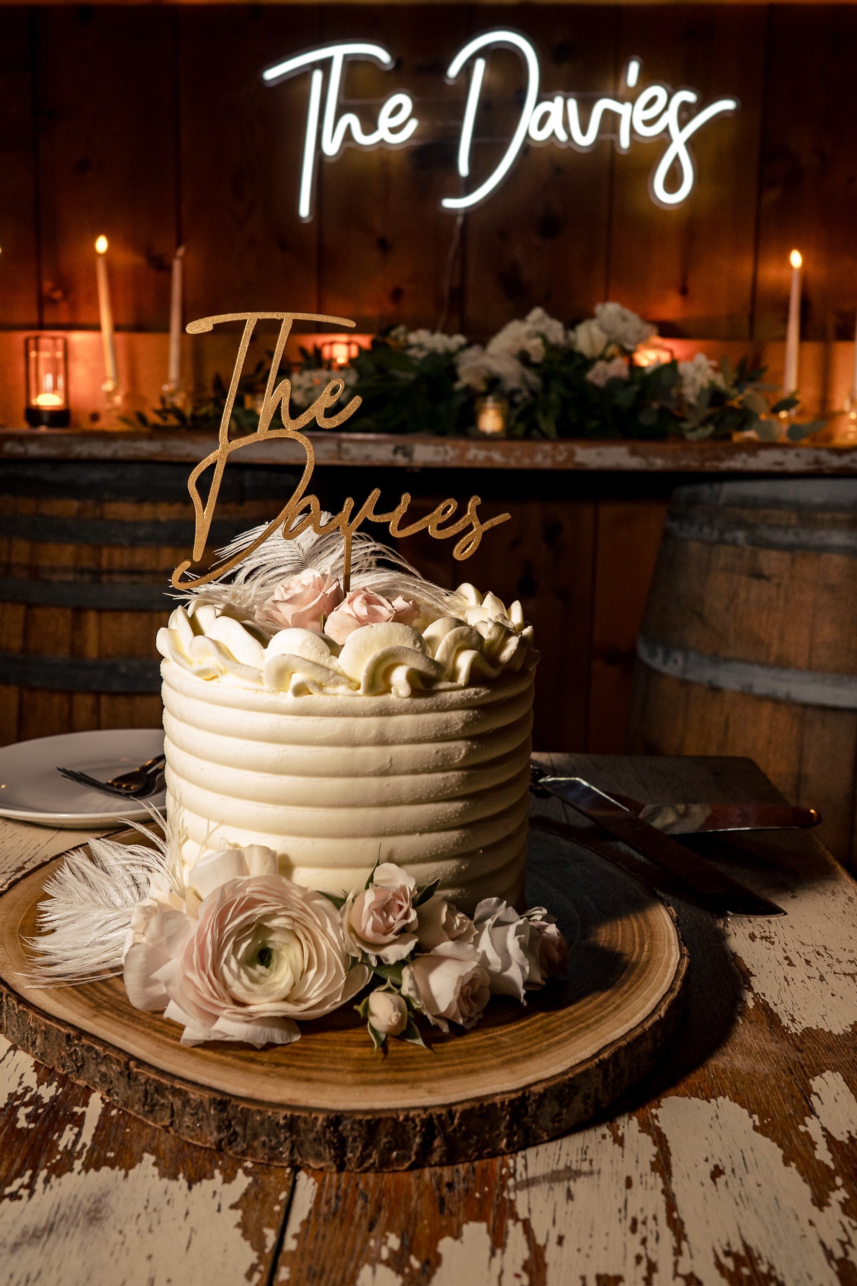 A flower-decorated wedding cake sits in front of a glowing reception sign.