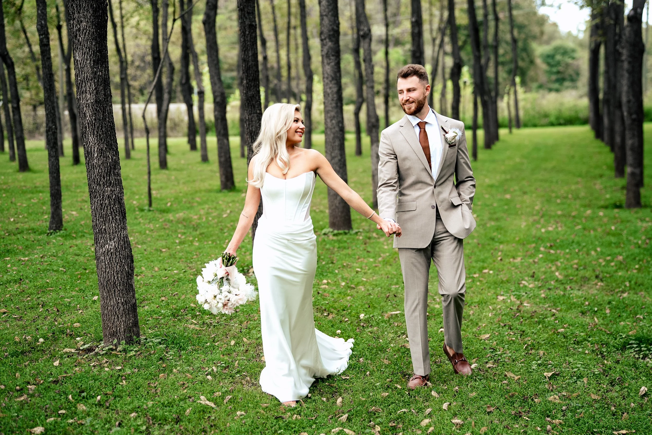 Ava and Jacob walk hand in hand across the grass between rows of trees.