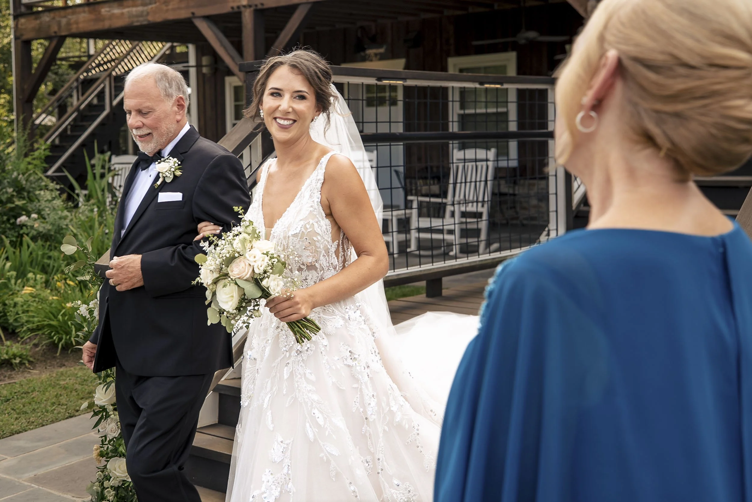Sarah smiling as she walks beside her father toward the outdoor wedding ceremony.