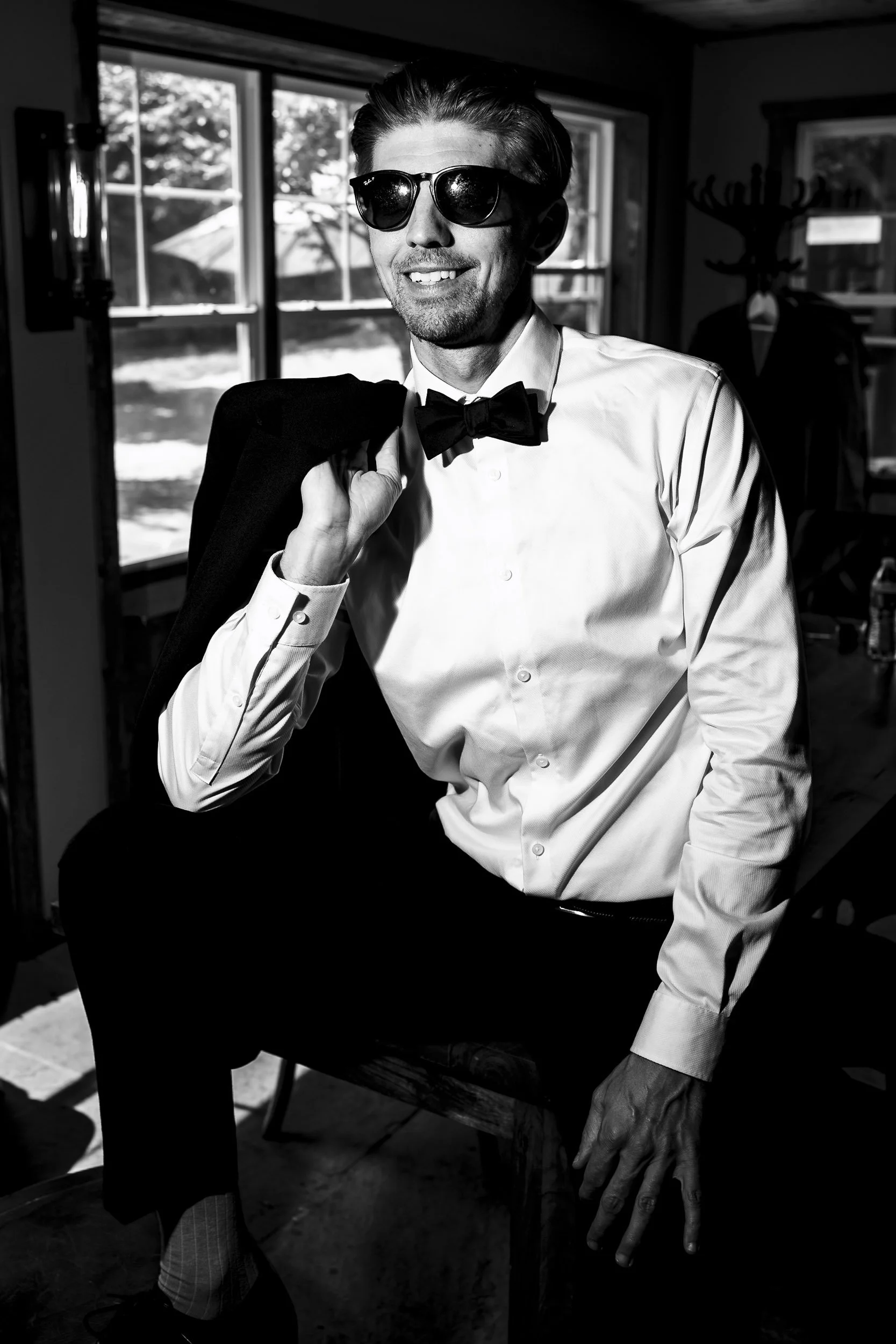 Black and white portrait of Andrew wearing sunglasses and a bow tie, with his suit jacket over his shoulder.