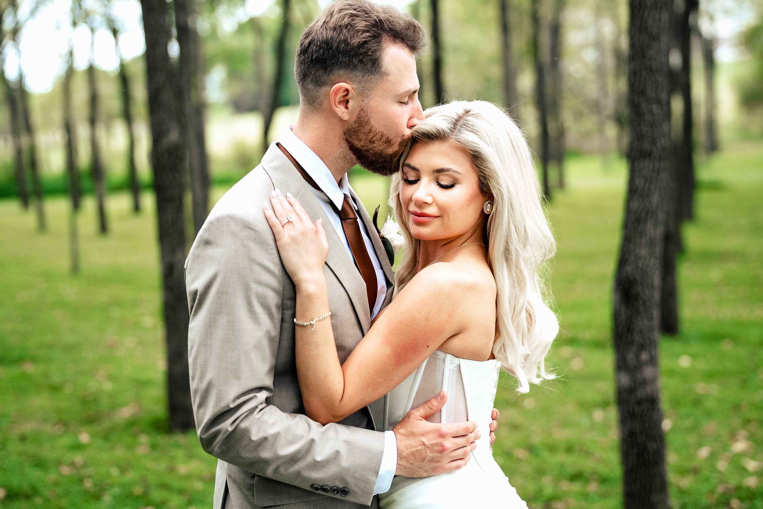 Jacob kisses Ava’s forehead as she closes her eyes during a portrait among the trees.