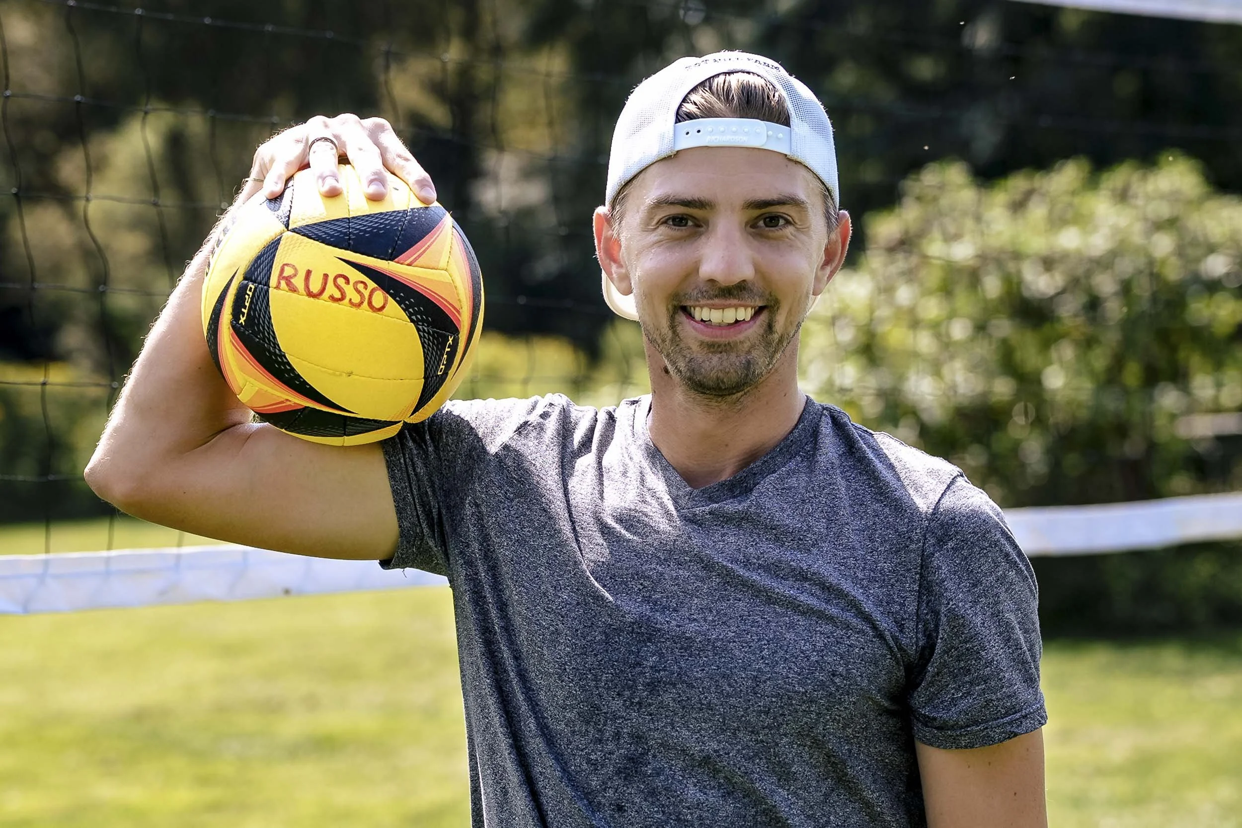 Andrew smiling with a volleyball resting against his shoulder before getting dressed for his wedding.