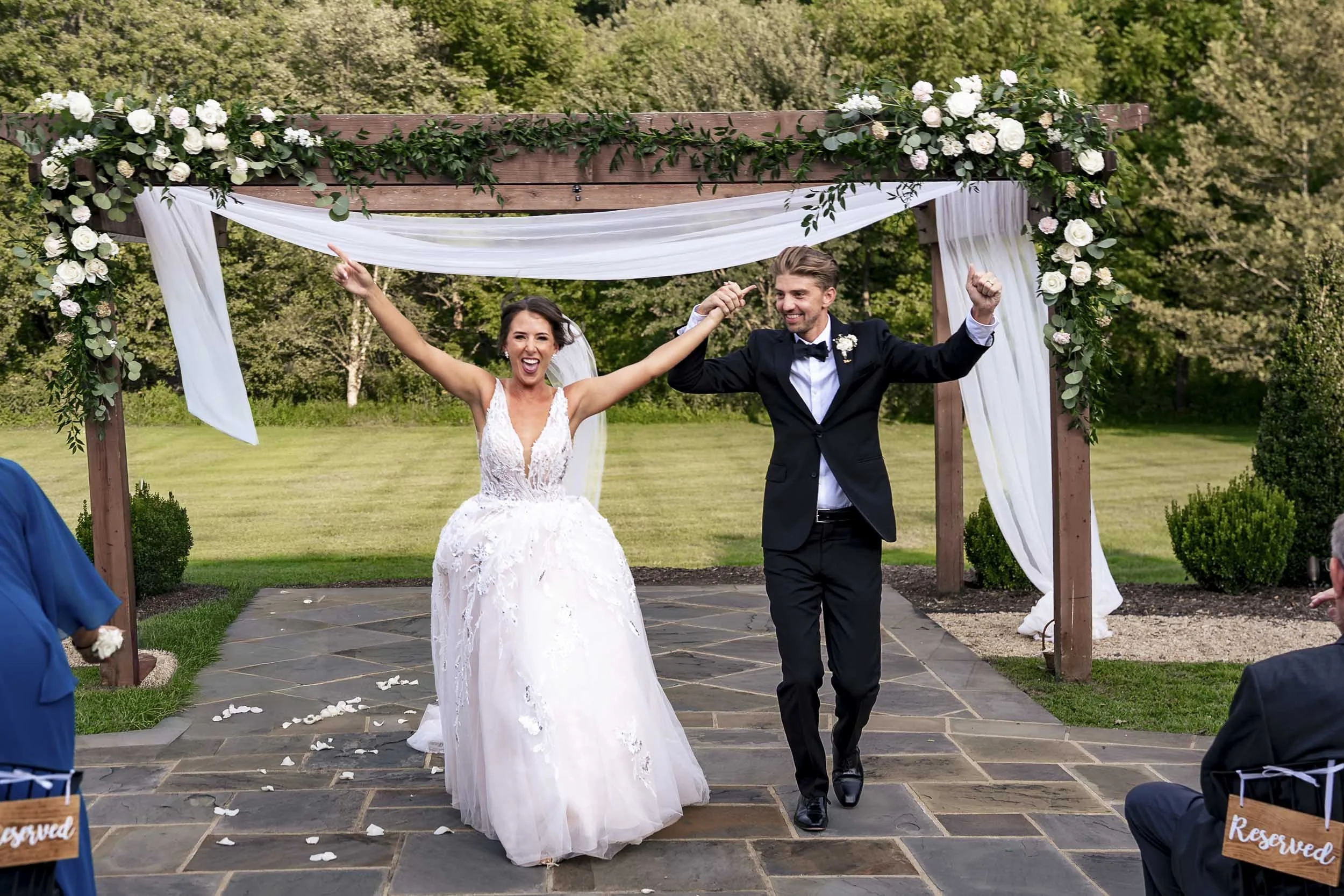 Sarah and Andrew raising their arms as they walk down the stone aisle after their outdoor ceremony.