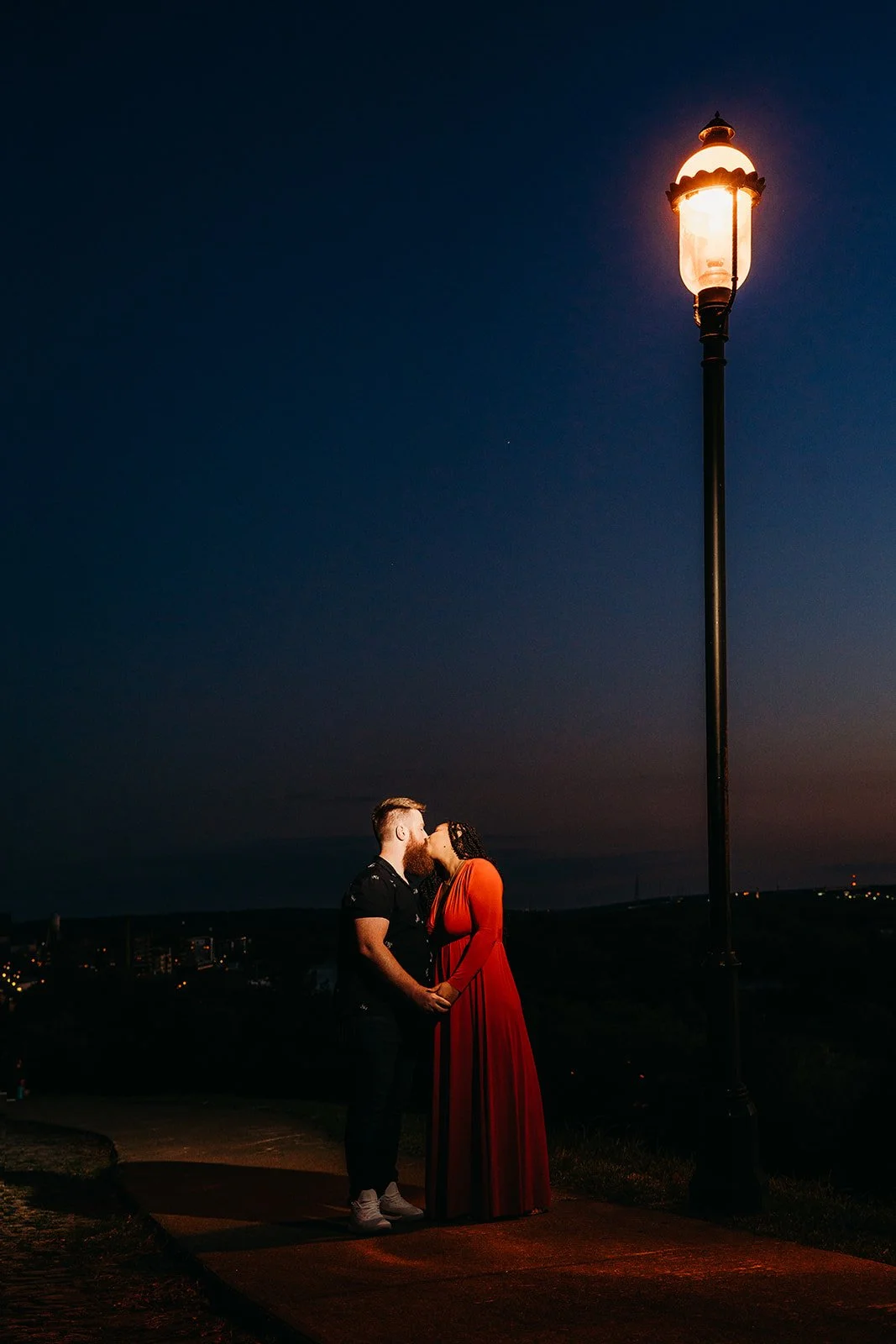 Ginay and Colin embracing beside a glowing park lamp during their October engagement session