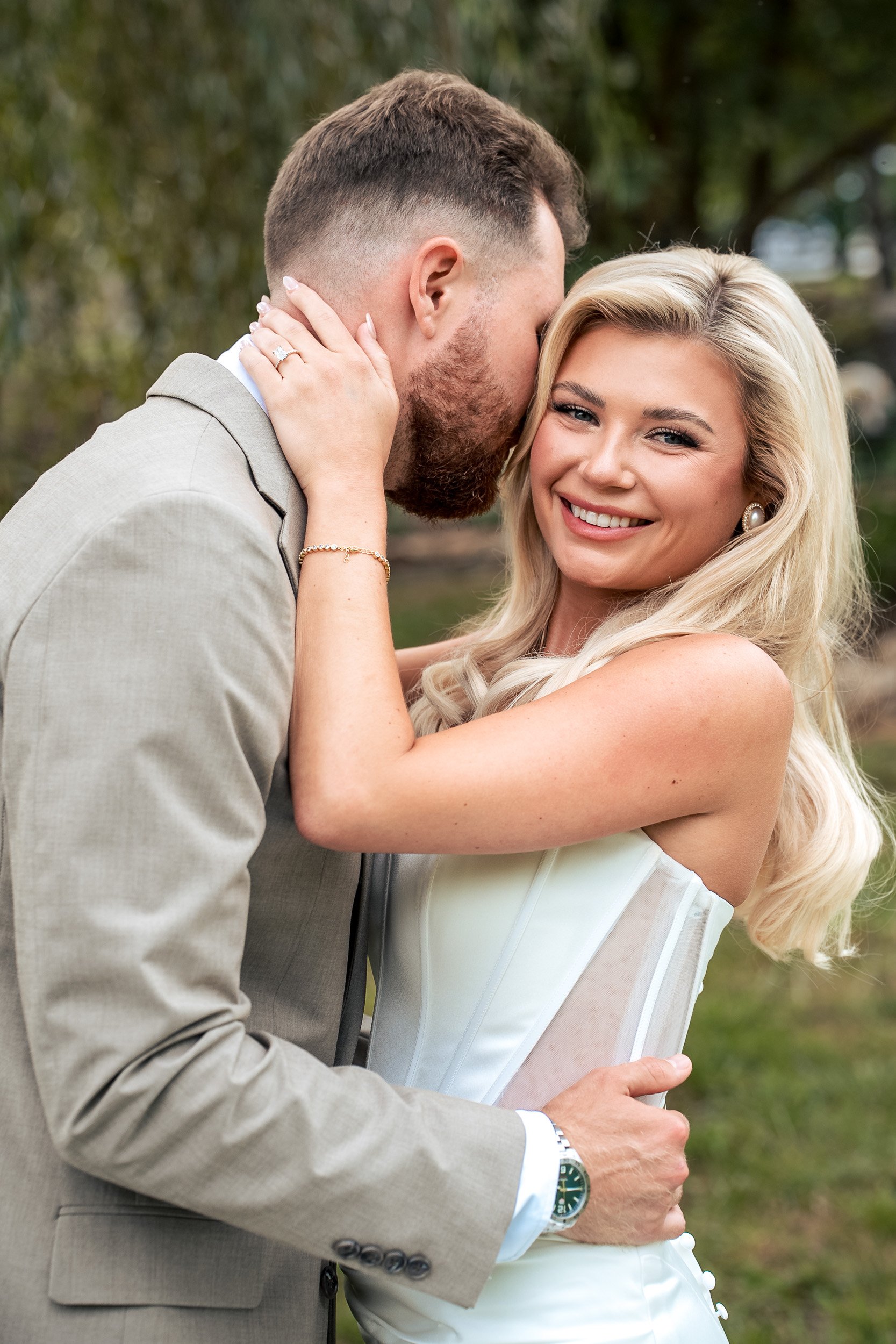Ava smiles while Jacob leans close during an outdoor wedding portrait.