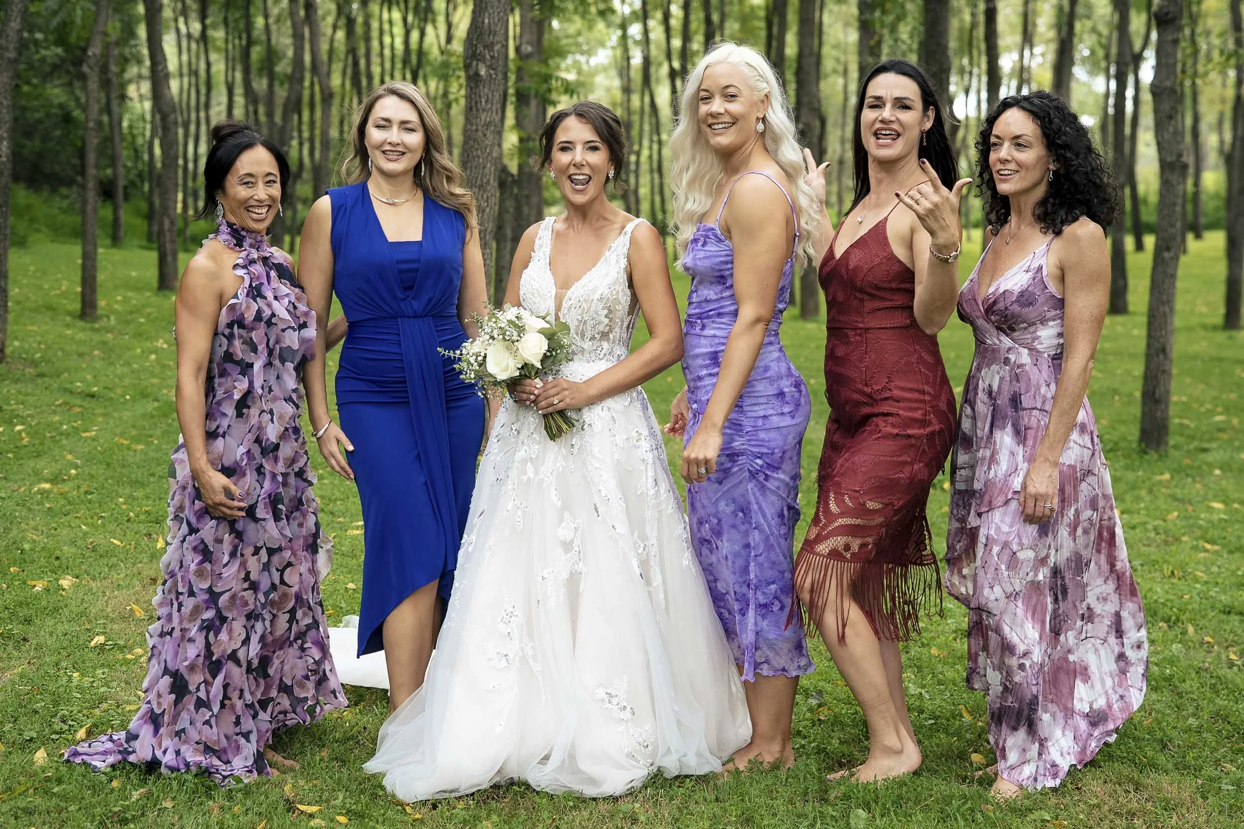 Sarah holding her bouquet beside bridesmaids wearing blue, purple, burgundy, and floral dresses.