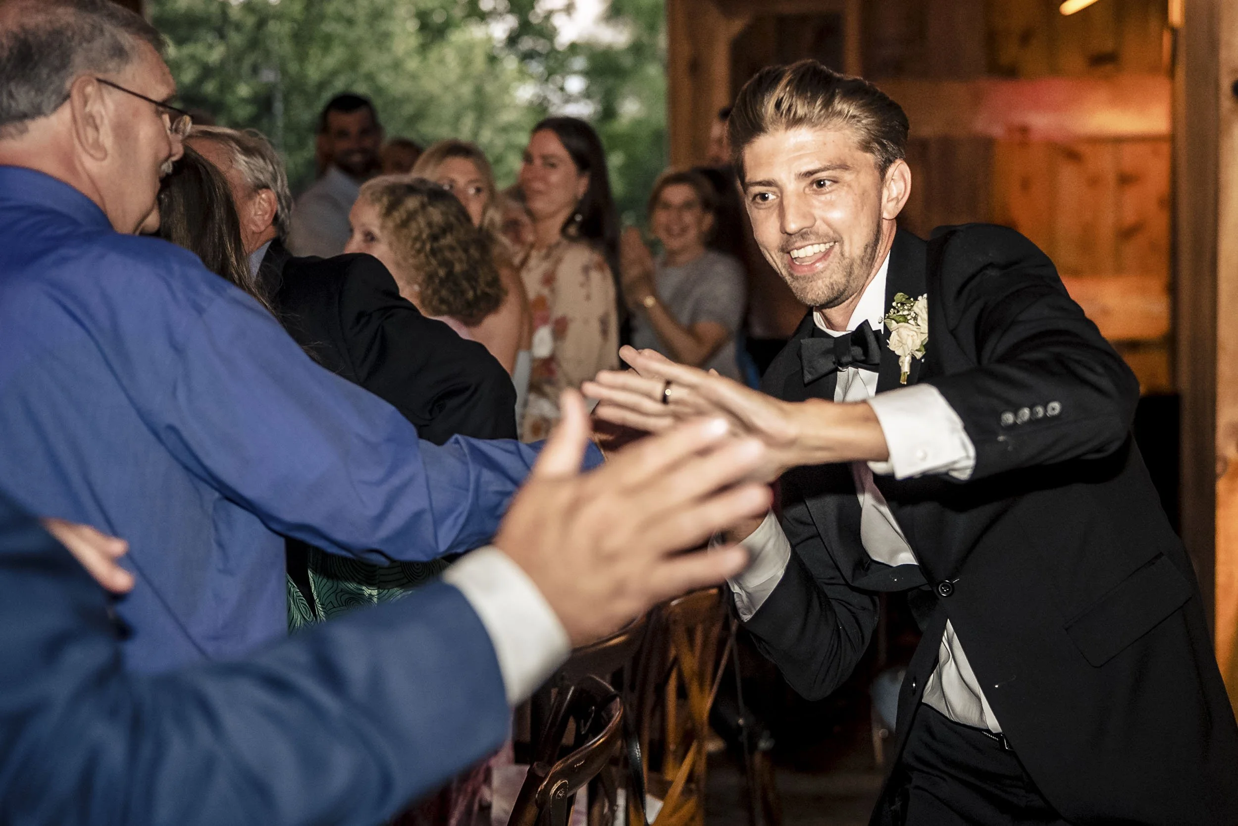 Andrew grinning and reaching toward guests’ outstretched hands during the wedding reception.