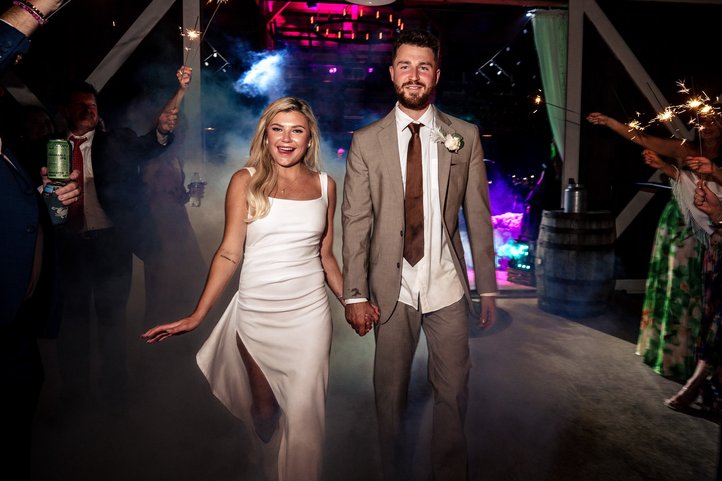 Ava and Jacob walk hand in hand between guests holding sparklers at night.
