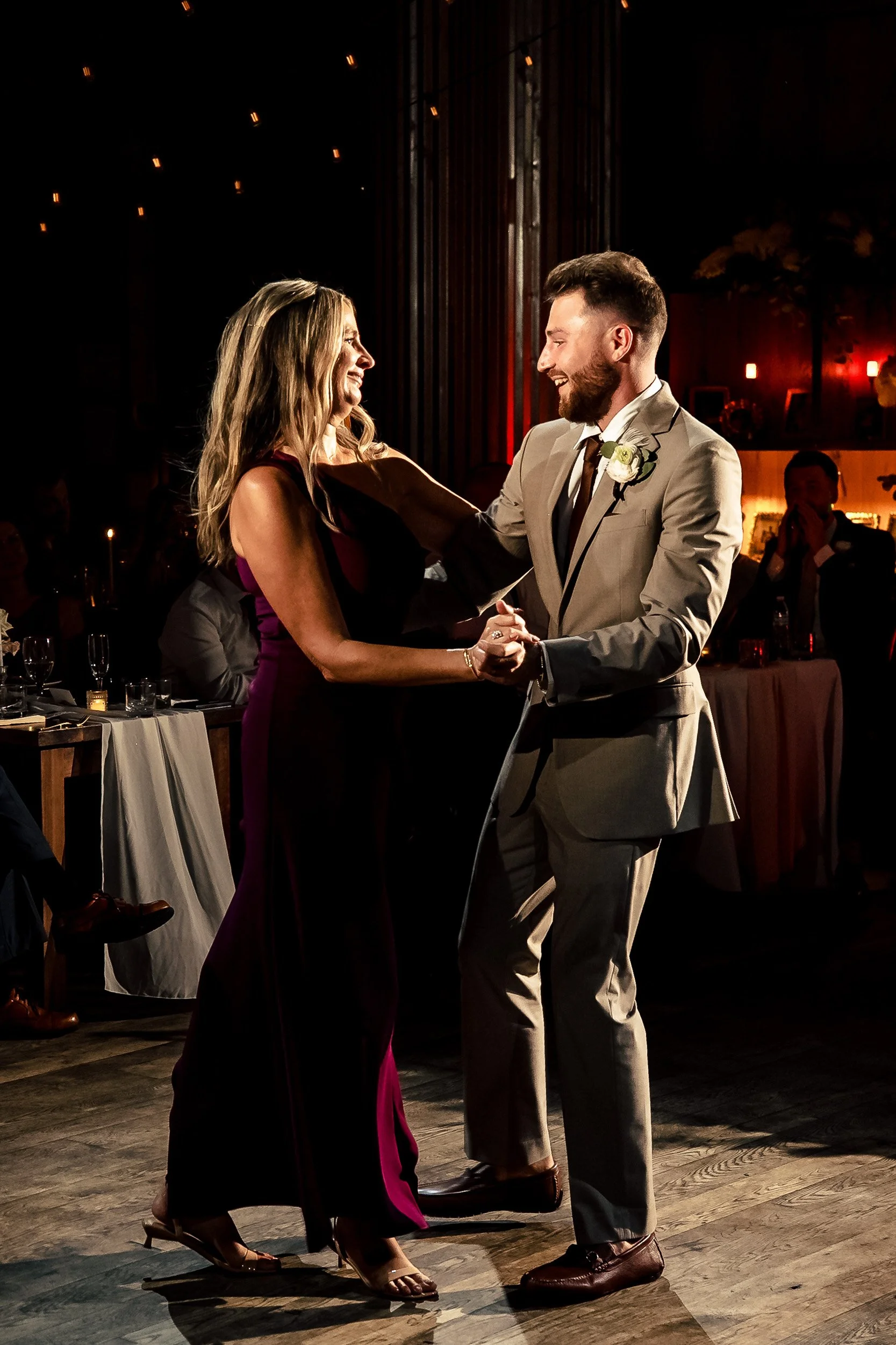 Jacob smiles while dancing with his mom in a dark dress at the reception.