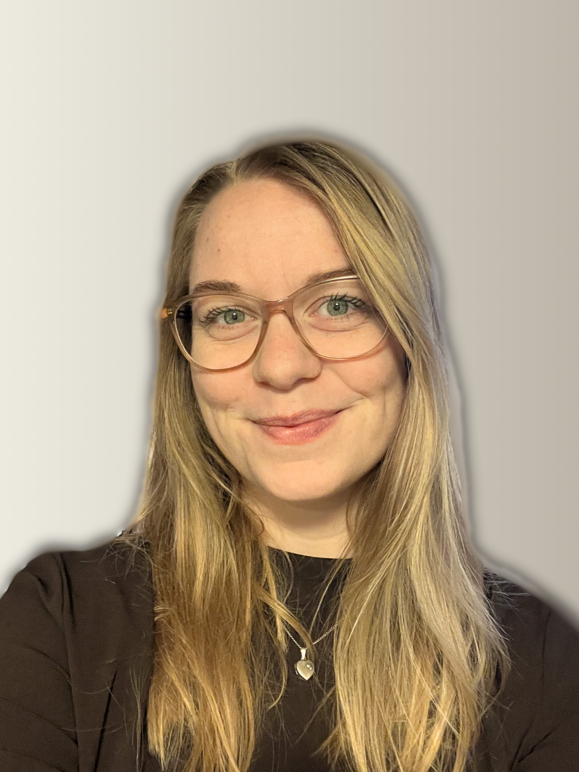 A woman with blonde hair, glasses, and a black shirt smiling at the camera, with a plain gray background.