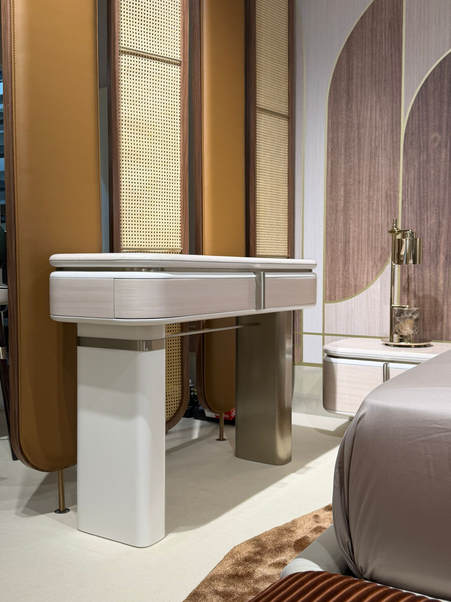 Luxury furniture exhibition stand at Salone del Mobile featuring a mid-century modern dining room, a fluted wood private bar with marble accents, and a sculptural chair gallery in a warm, textured interior.