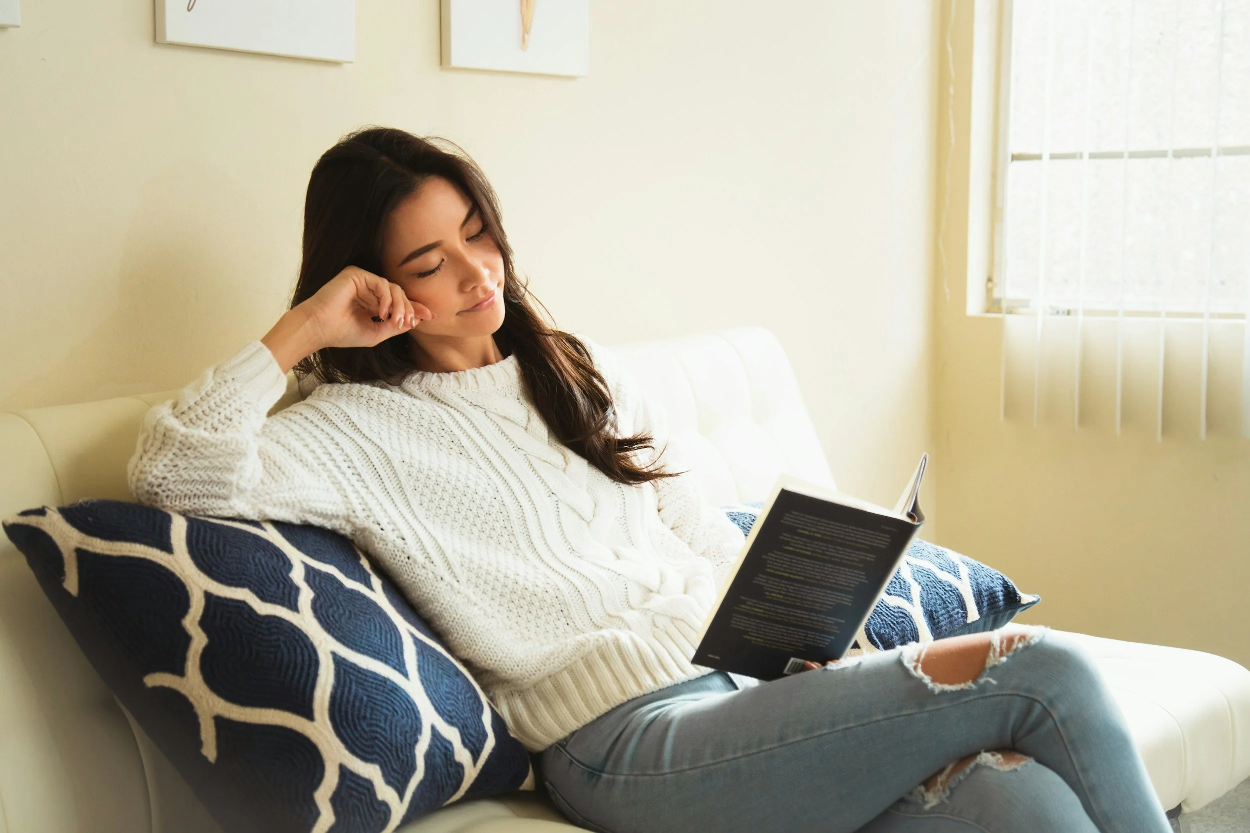 Woman on couch reading book.