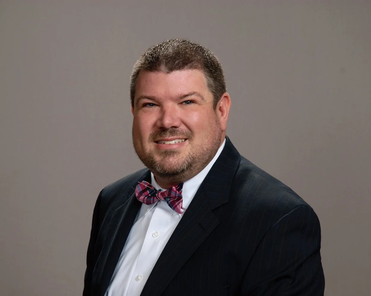 A man with dark hair and a beard, wearing a dark suit with a bow tie, smiling at the camera.