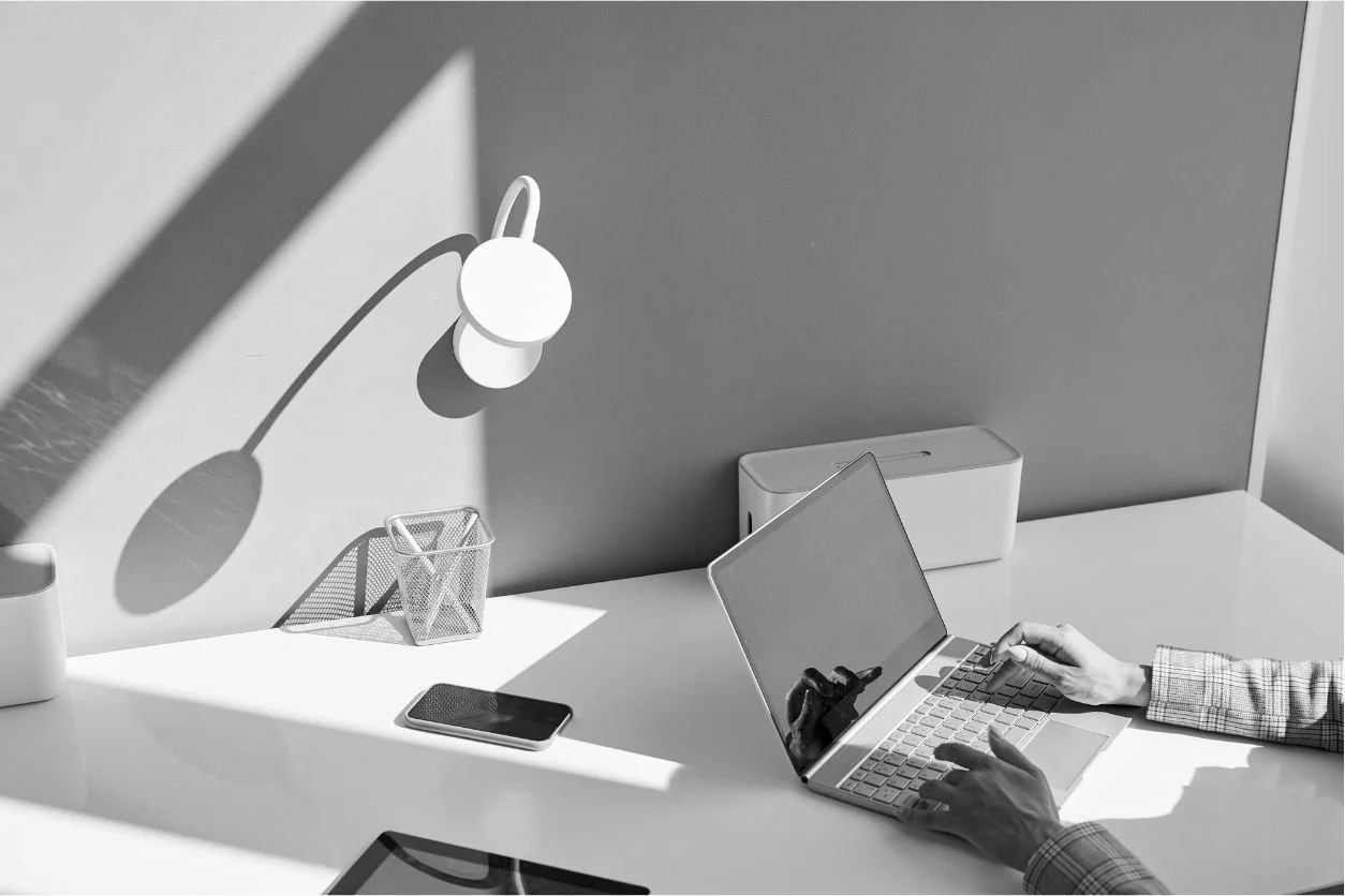 A minimalist desk with a laptop, phone, and lamp, suggesting a quiet workspace and unfinished tasks