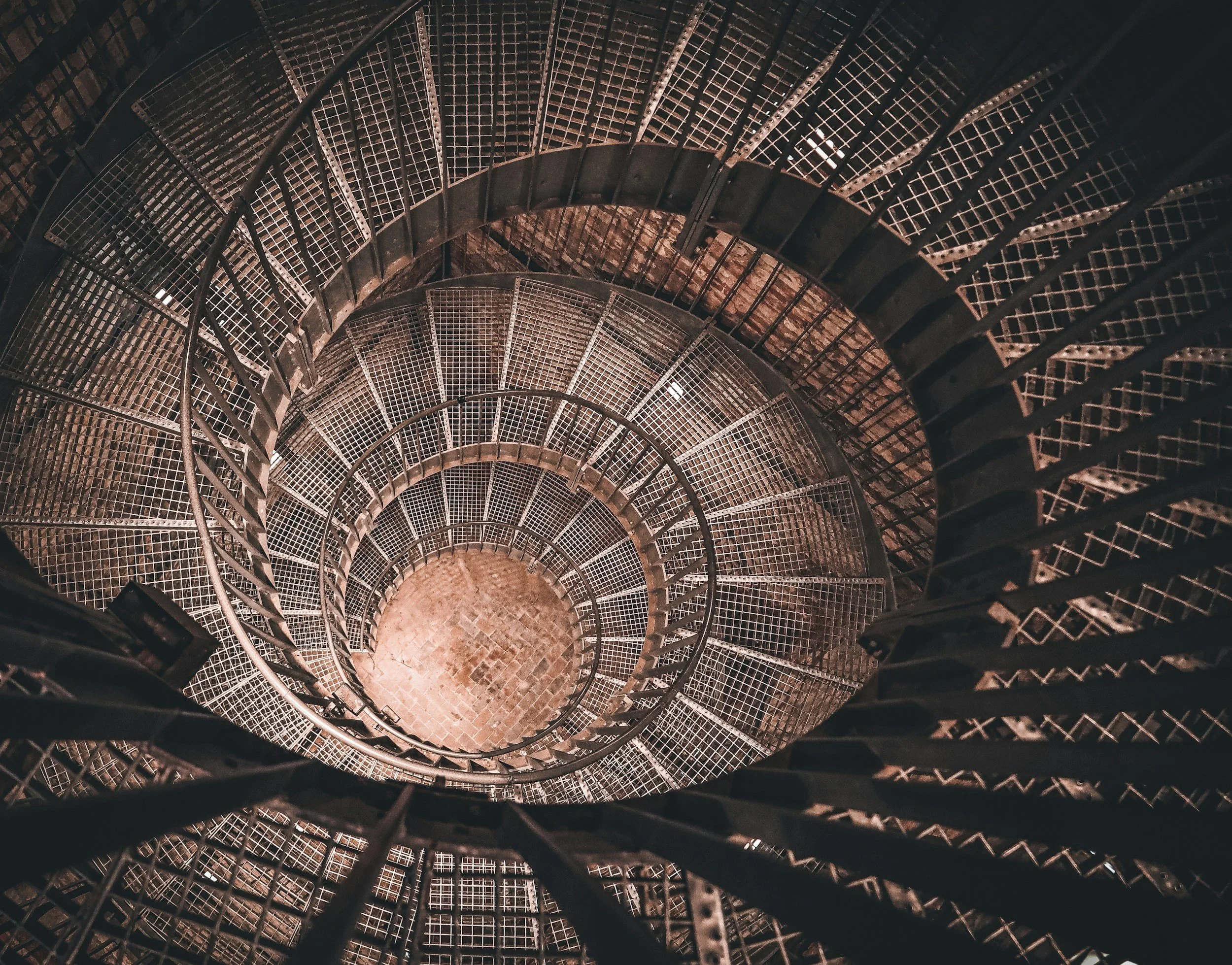Overhead photograph of a circular metal spiral staircase viewed from above, showing layered levels and repeating geometric patterns, reflecting the depth and complexity of ADHD across the lifespan.