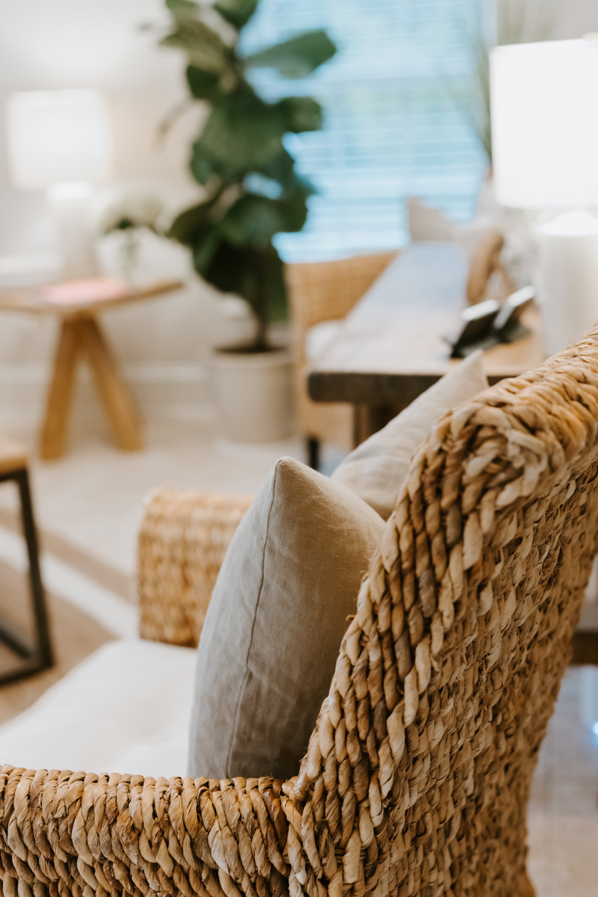 Close-up of a woven rattan armchair with beige cushions in a cozy, well-lit living room.