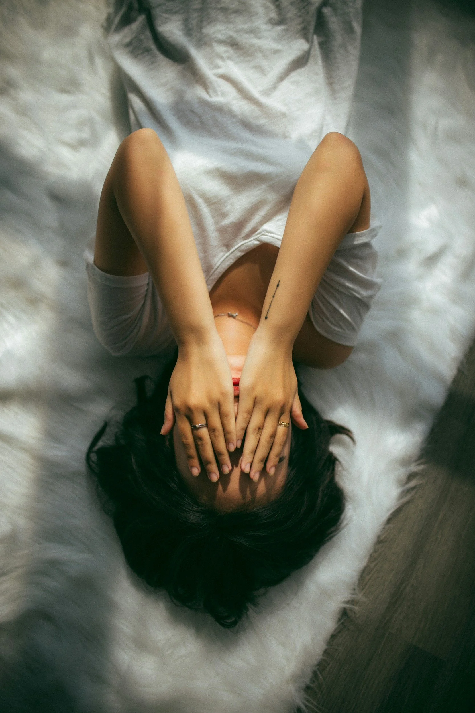 Upside down photo of a woman lying on bed with her hands hiding her face
