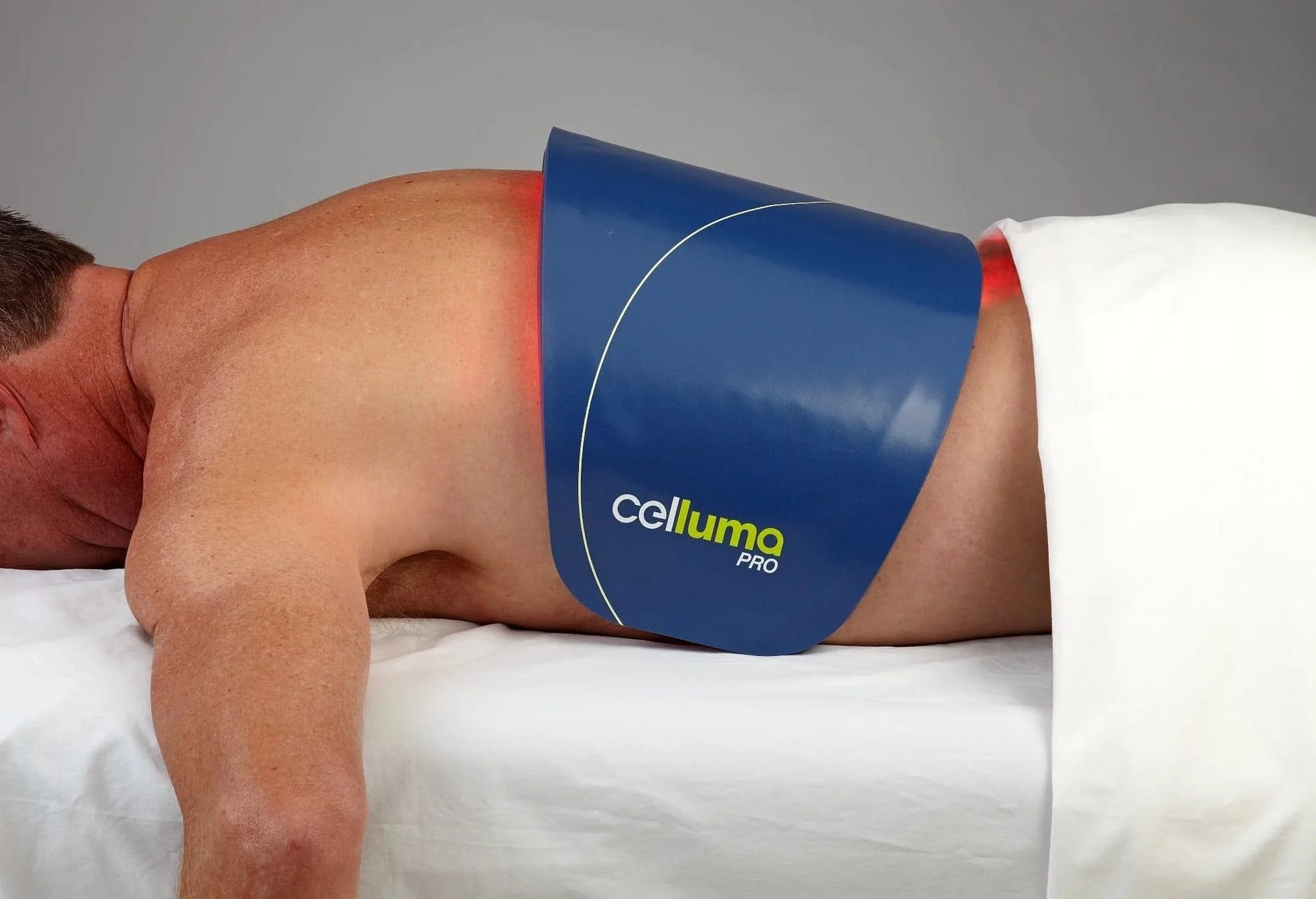 A person lying face down on a white bed with a blue medical device on their back labeled 'Celluma PRO'.