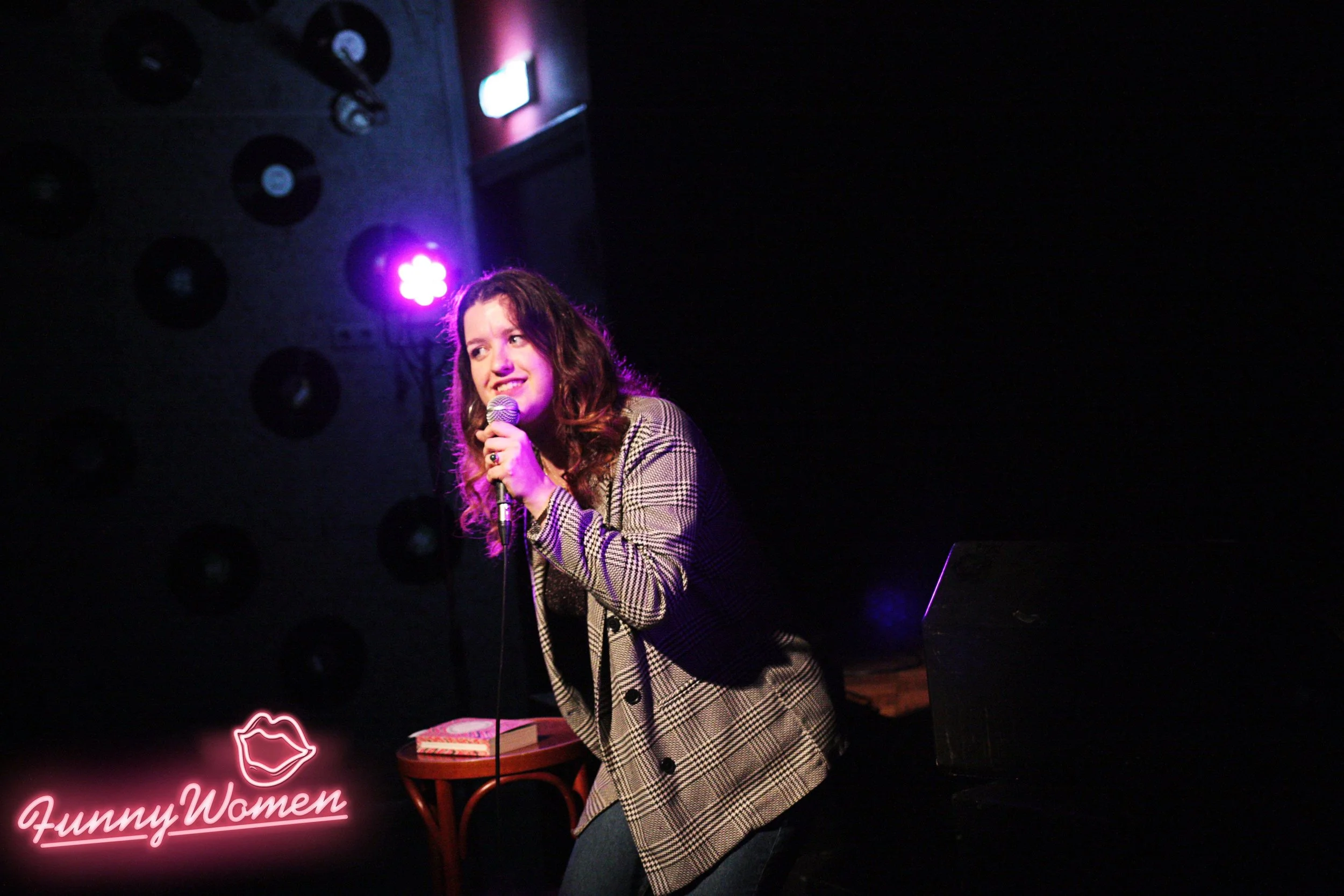 Julie Kasinski performing on stage at a comedy event under vibrant lighting.