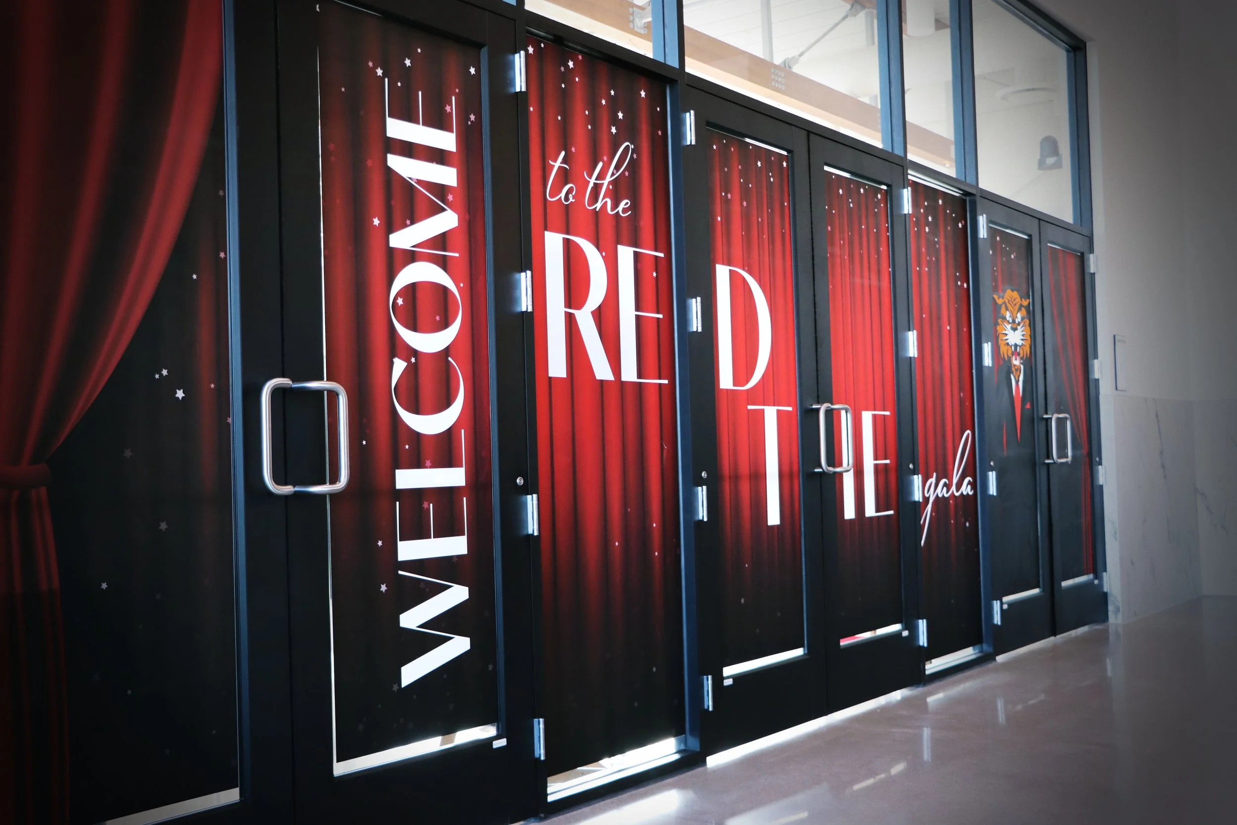 Entrance of a Red Gala event, with a black door decorated with red curtains and stars, and the words "Welcome to the Red Gala" in white lettering.