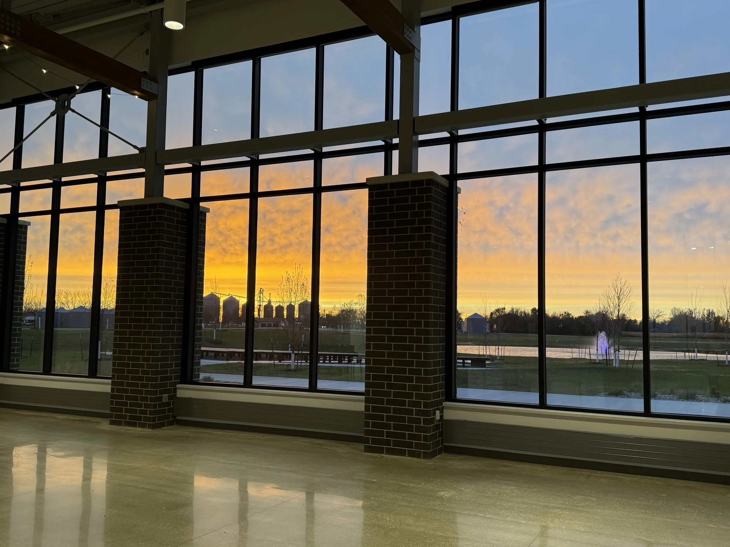 Sunset view through large window panels of an indoor space with brick supports and a polished floor.