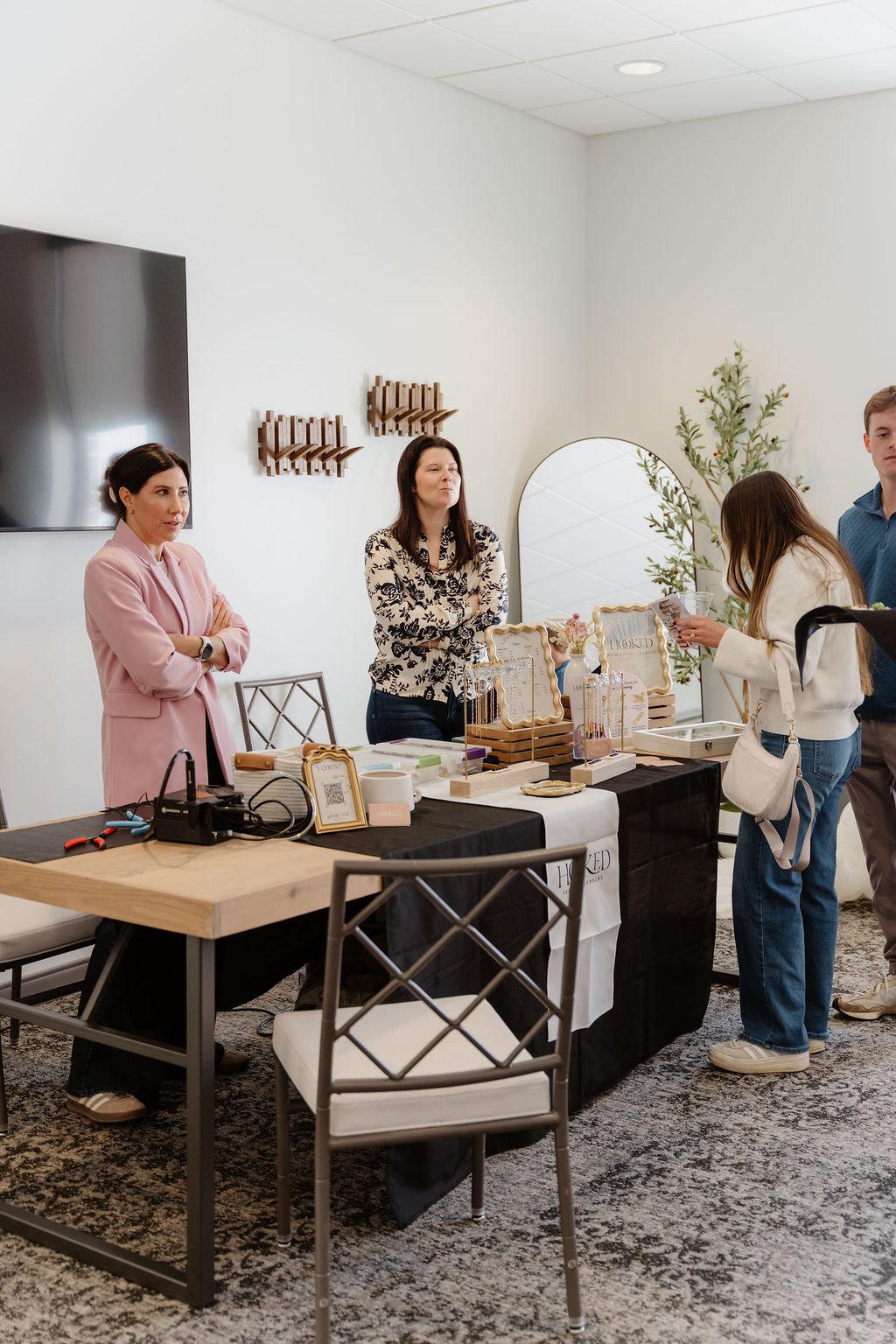 People at a market table with jewelry and handmade crafts at an indoor event.