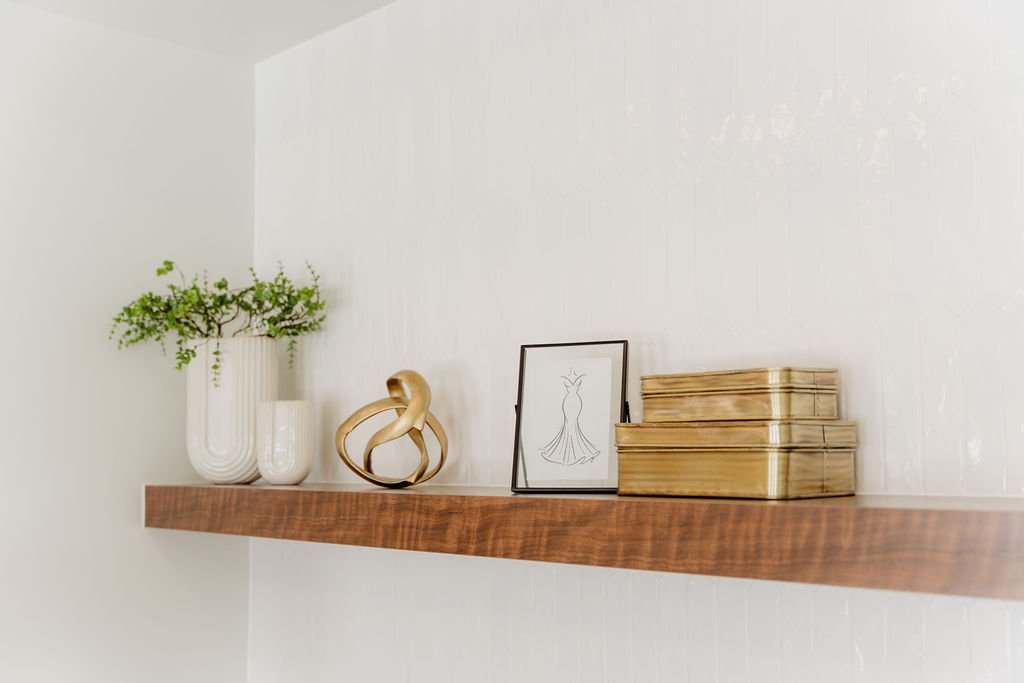 Decorative shelf with white vases, a gold knot sculpture, a framed fashion sketch, and stacked boxes on a plain wall.