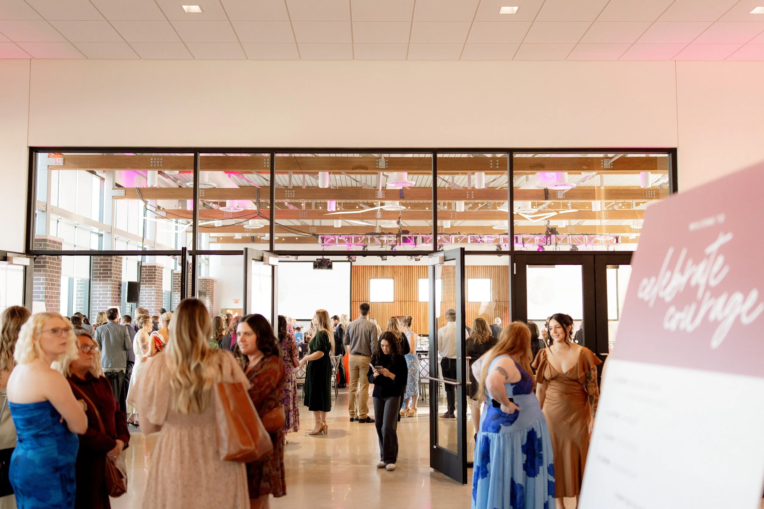 People attending an indoor event or conference, gathered in a spacious, modern room with high ceilings and large windows.