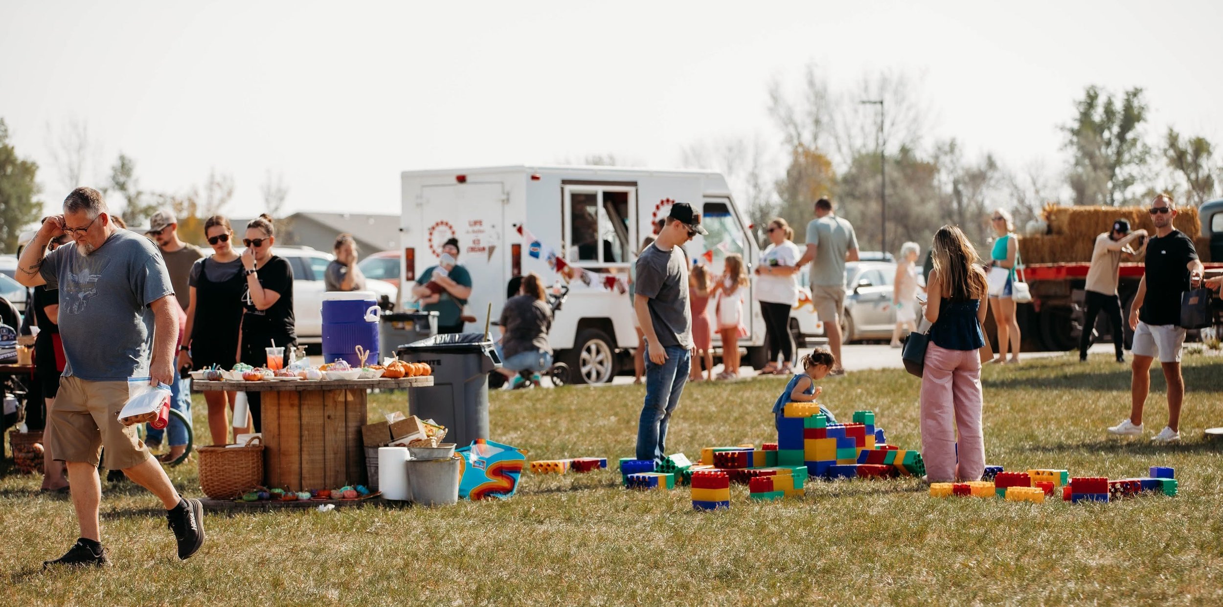 People at an outdoor fair with food trucks and children's toys on a grassy field.