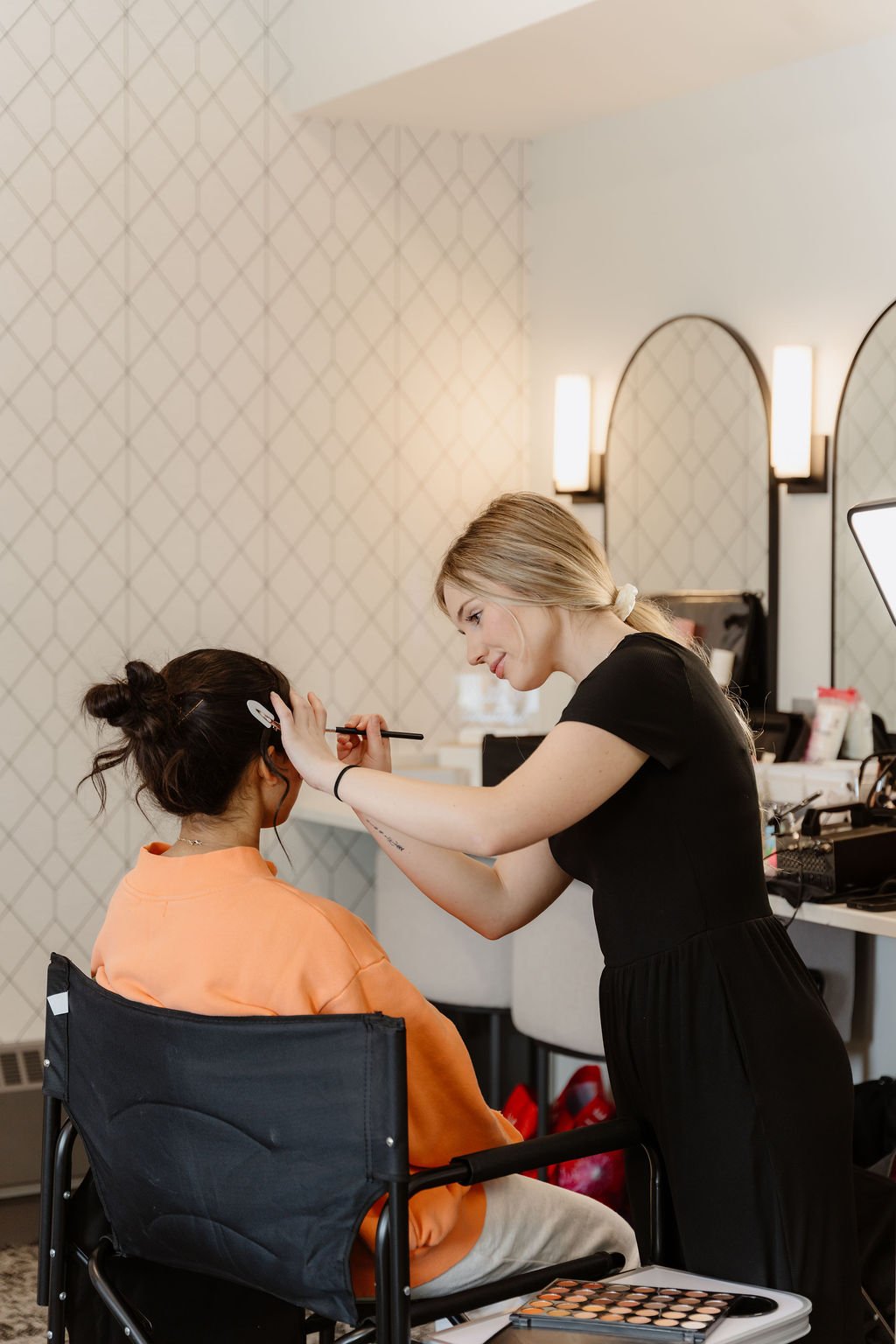 Makeup artist applying makeup to a woman seated in a chair.