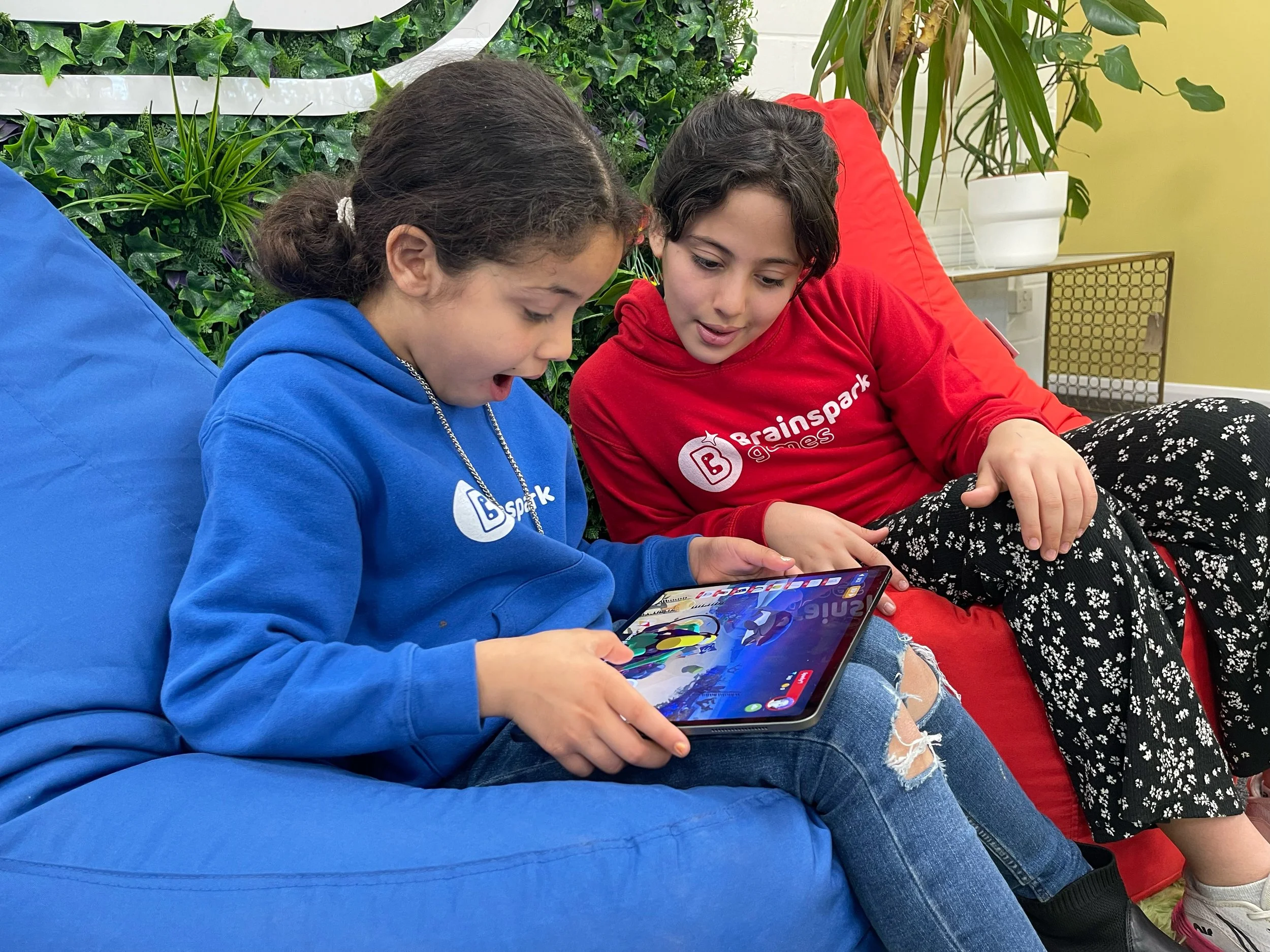 Two young girls sitting on a blue beanbag, one wearing a blue hoodie and the other wearing a red