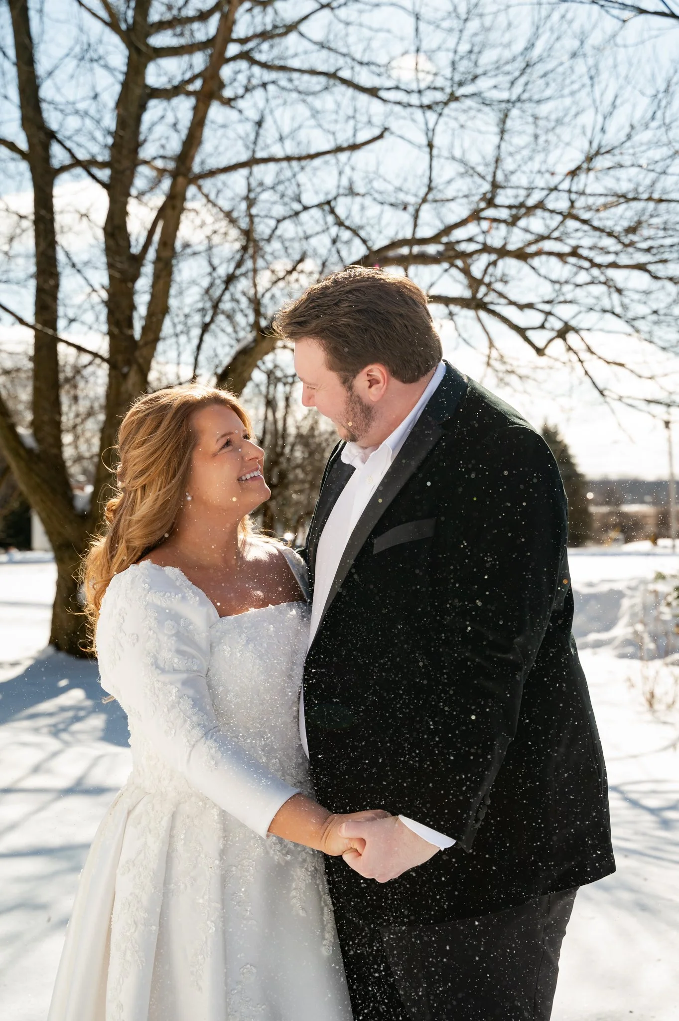 A Bride and Groom smiling and holding onto each other as snow falls.