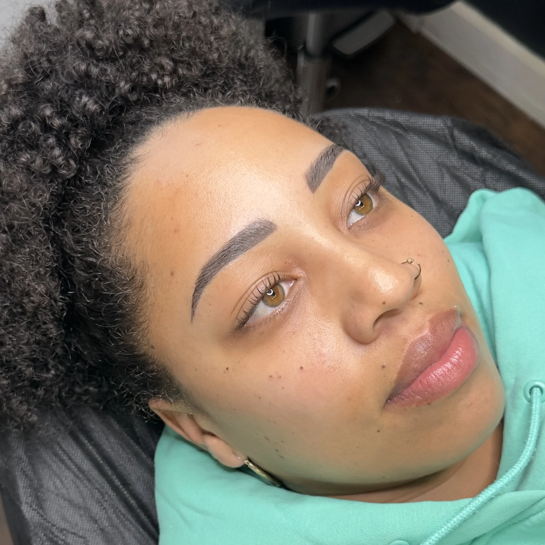 Close-up of a woman with clear skin, closed eyes, and a gold nose ring, lying down.