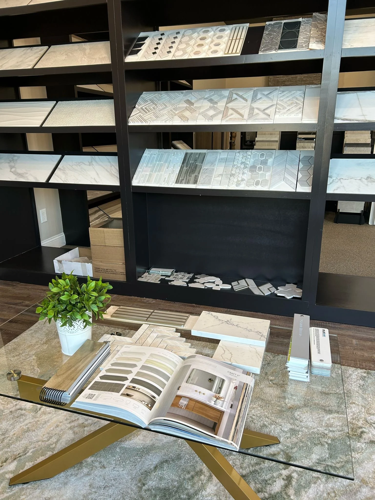 Display of various tile samples and a catalog on a glass table in a tile showroom.