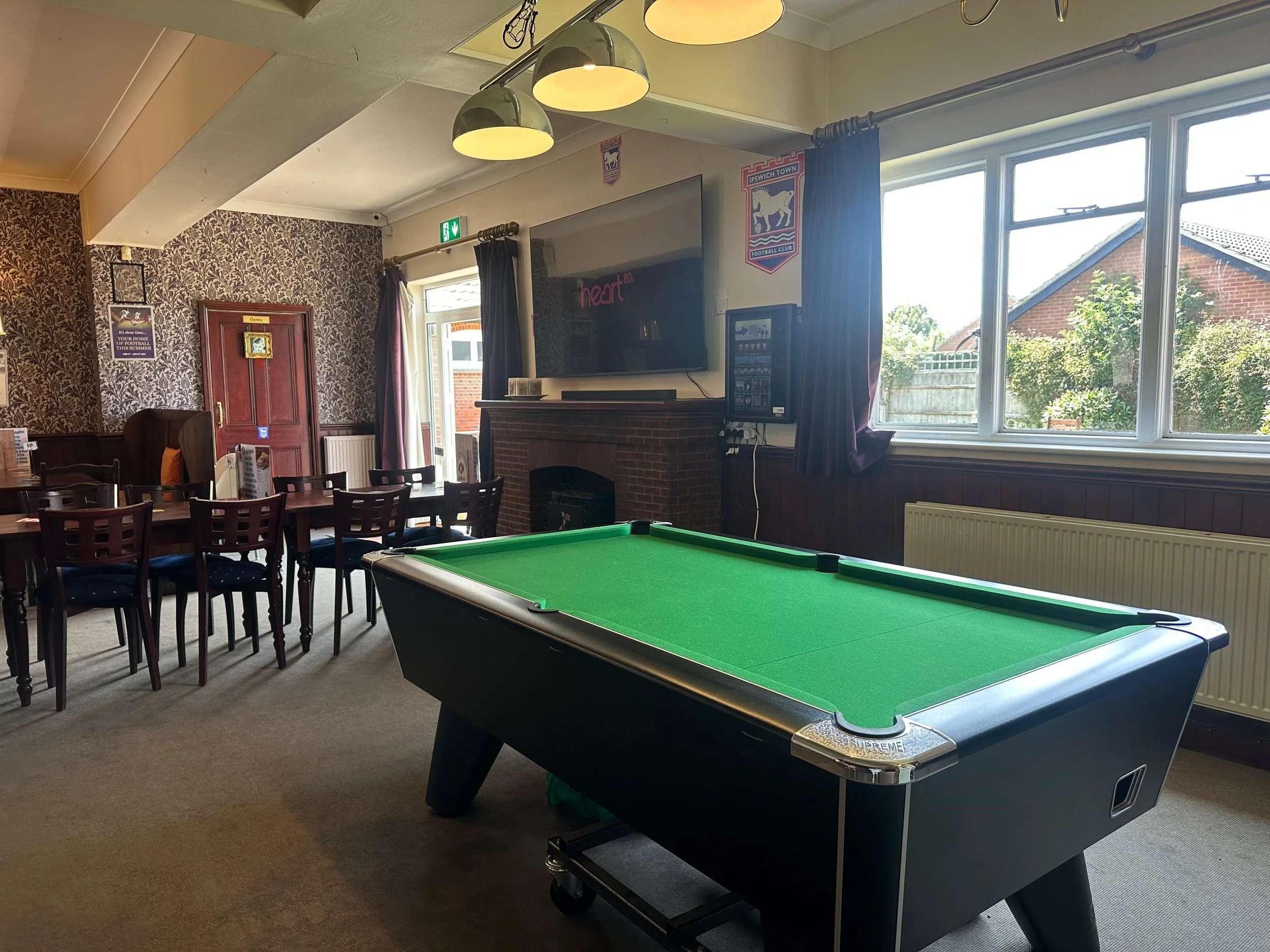 Indoor recreational room with pool table, dining area, wallpaper, television, and windows showing a garden outside.