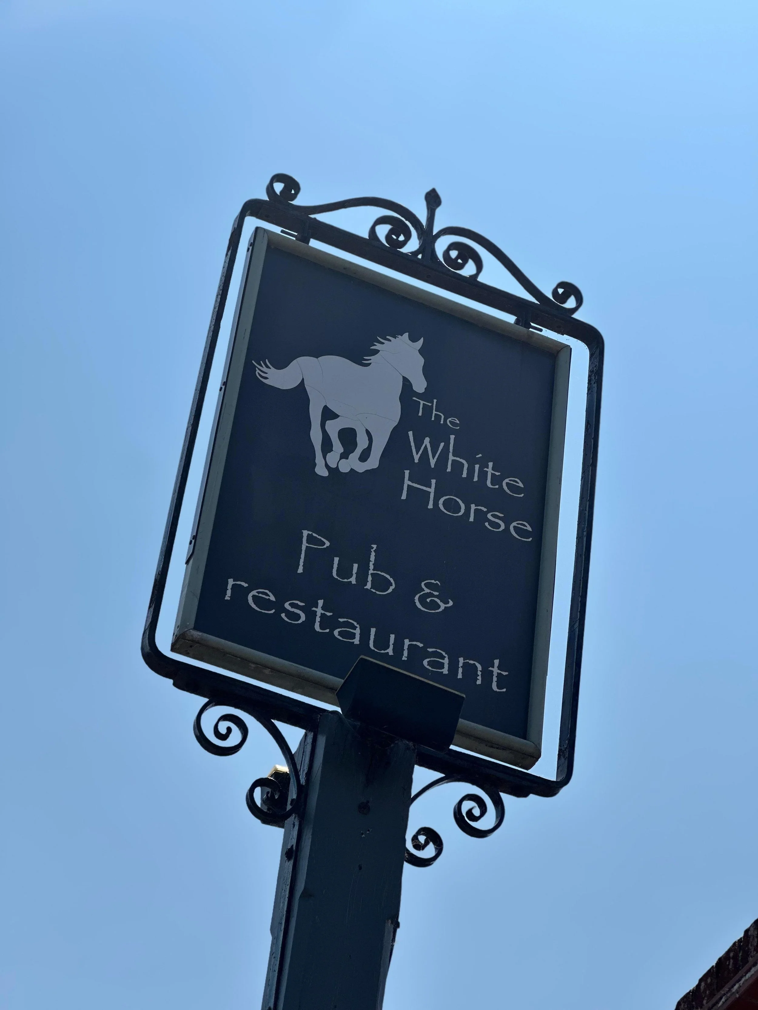 Sign for The White Horse Pub & Restaurant with a white horse graphic against a blue sky.