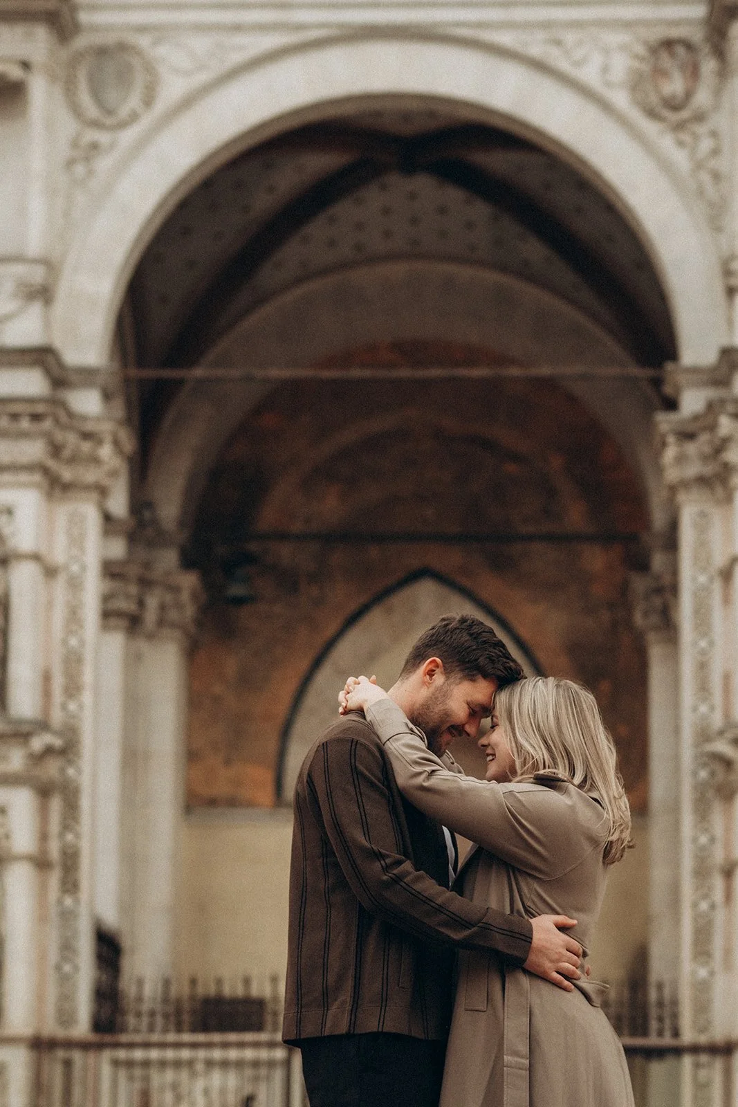 A couple hugging and smiling in front of an ornate architectural background in the city of Siena.