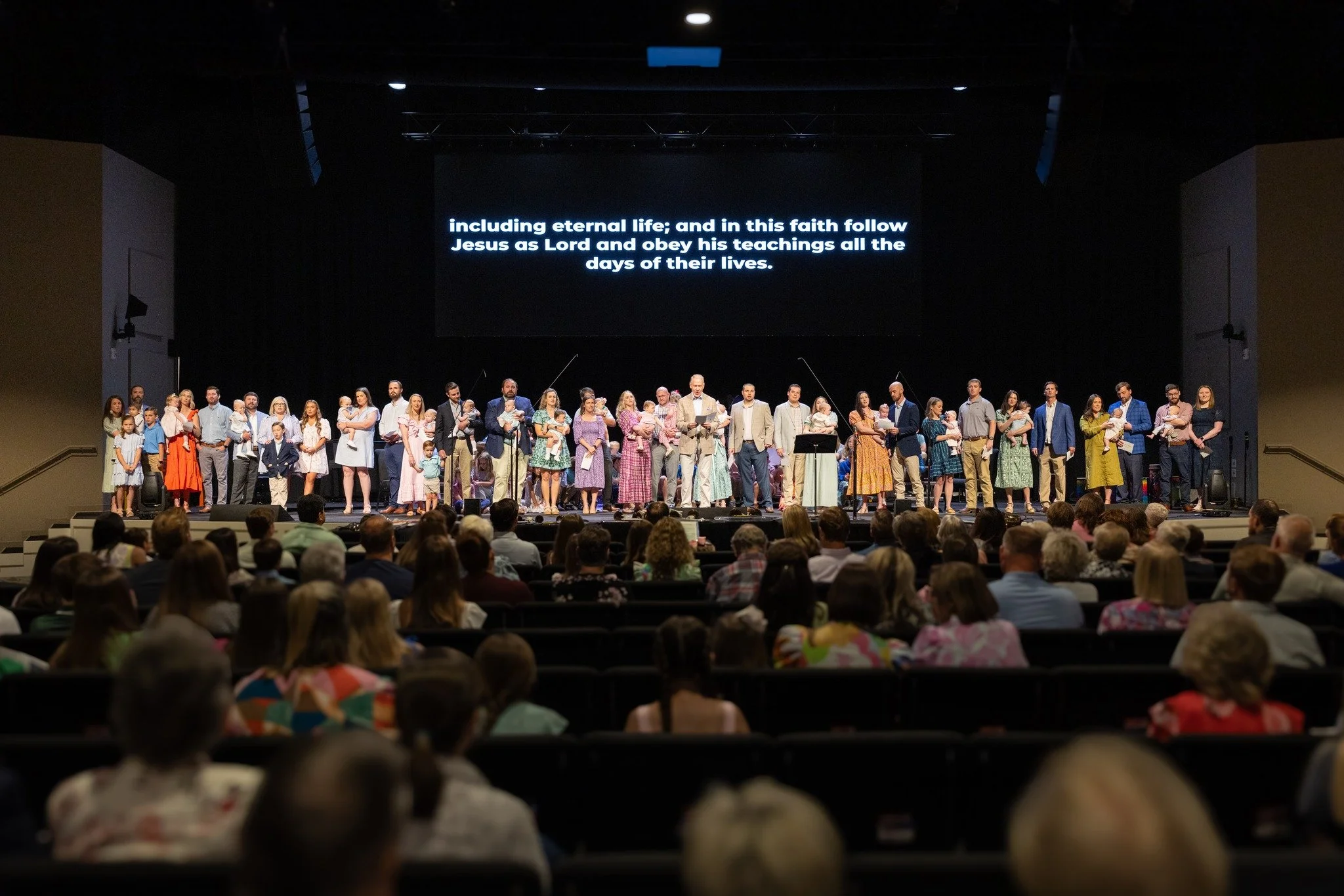 A large congregation watching a church service or concert on stage with a choir and soloists, in a theater or auditorium.