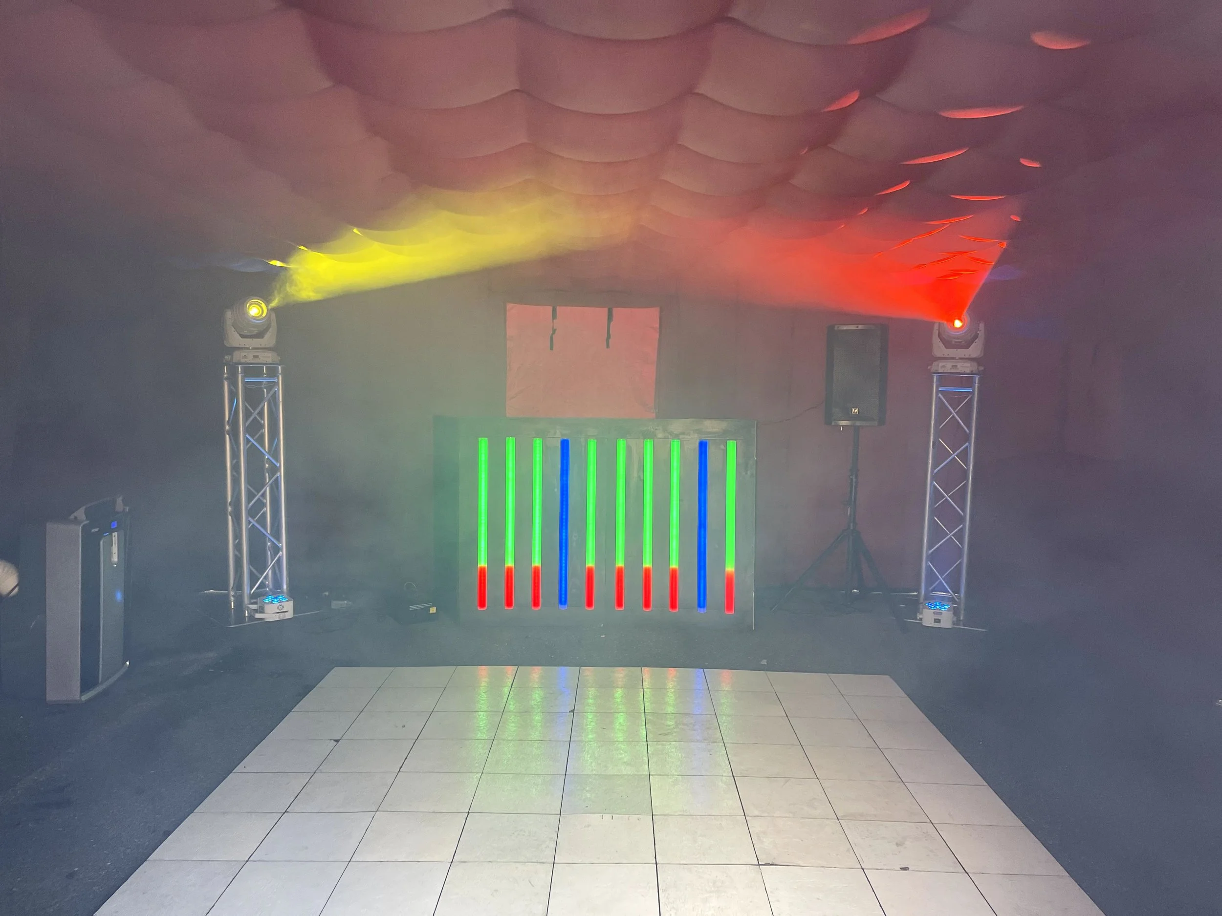Indoor party setup with colorful LED lights, a smoke machine, two light towers, and speakers on a tiled floor.