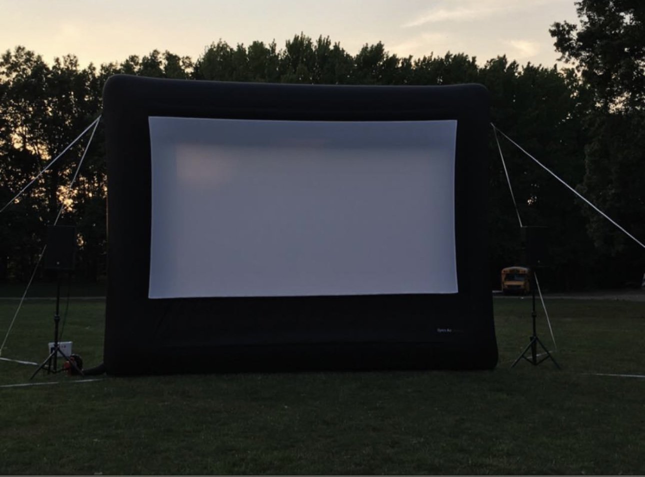 Inflatable outdoor movie screen set up on a grassy field with trees in the background.