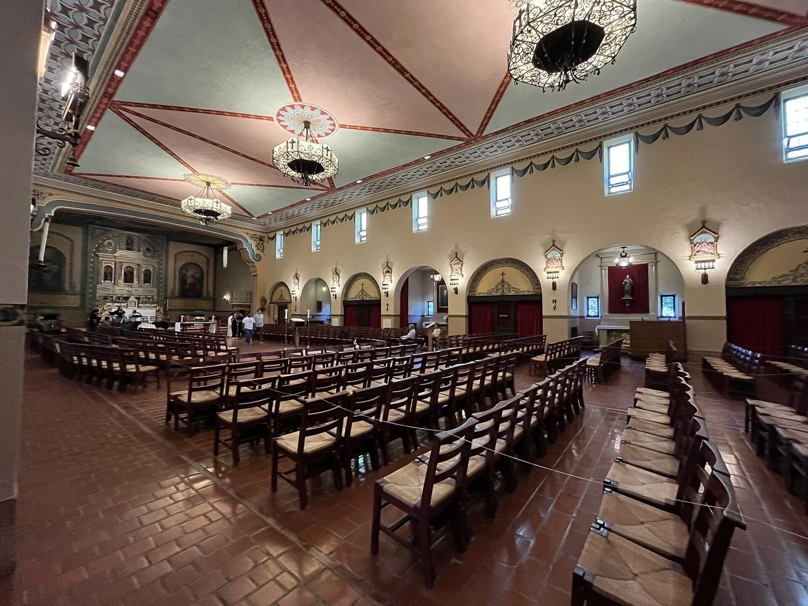 The interior of Mission Santa Clara de Asís, with rows of wooden pews leading to an ornate painted altar and ceiling.