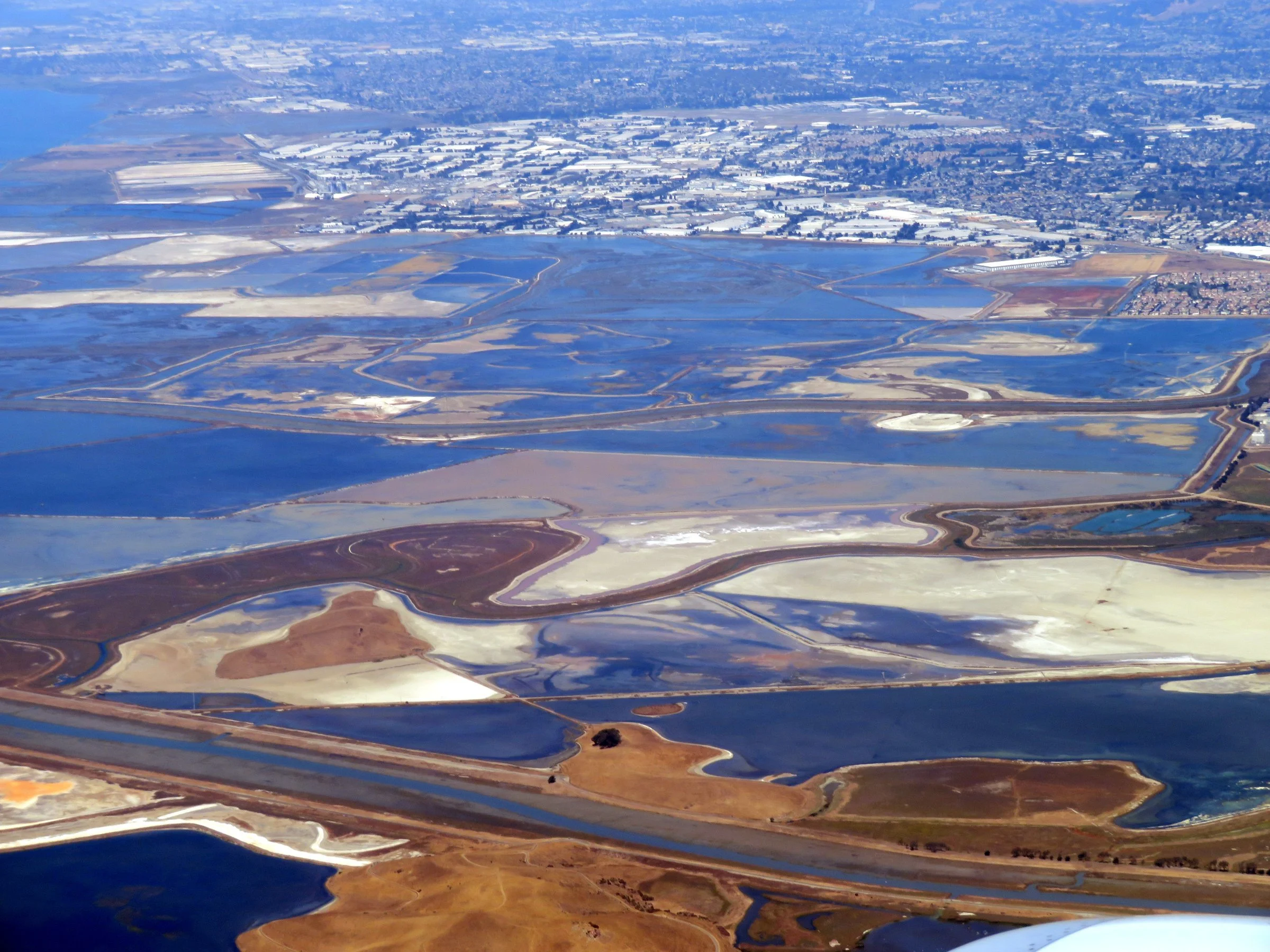 An aerial view of the Alameda Creek delta, with salt ponds in red, white and blue spreading toward the East Bay shoreline.