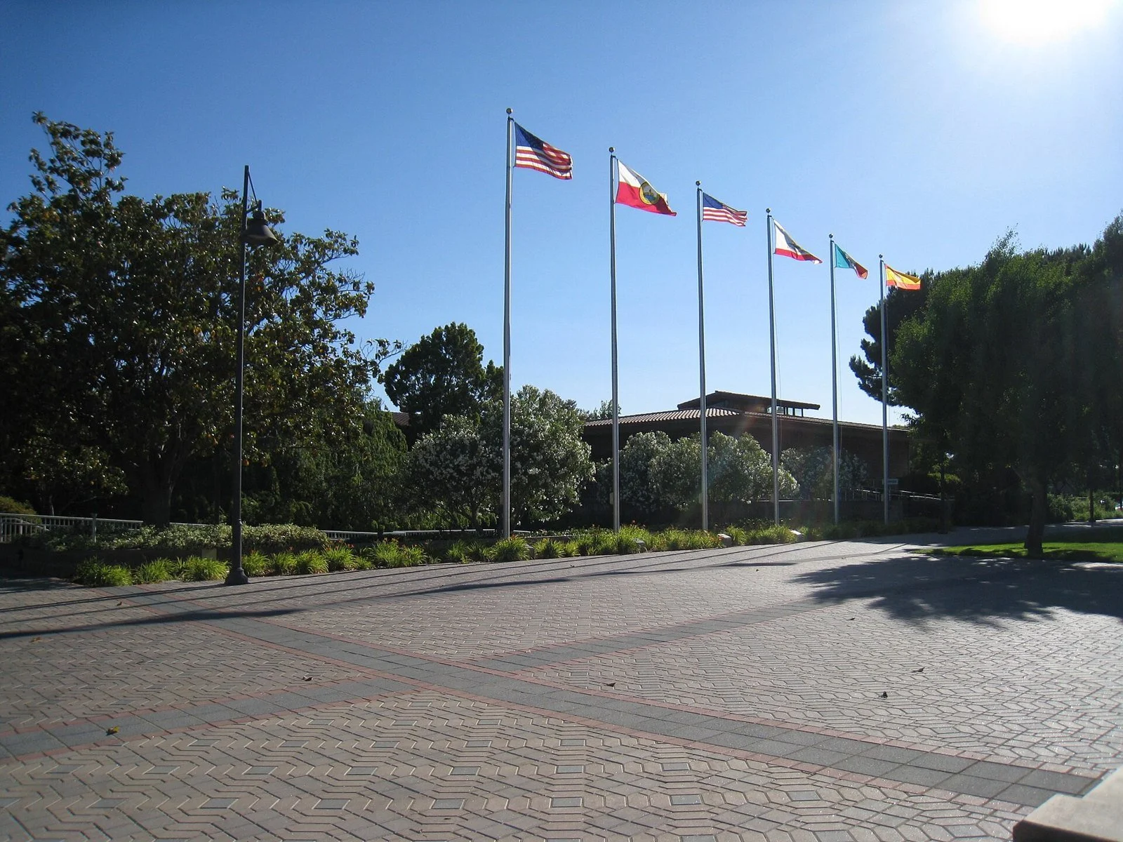 Flags on tall poles fly in front of the Santa Clara city hall building under a blue sky.